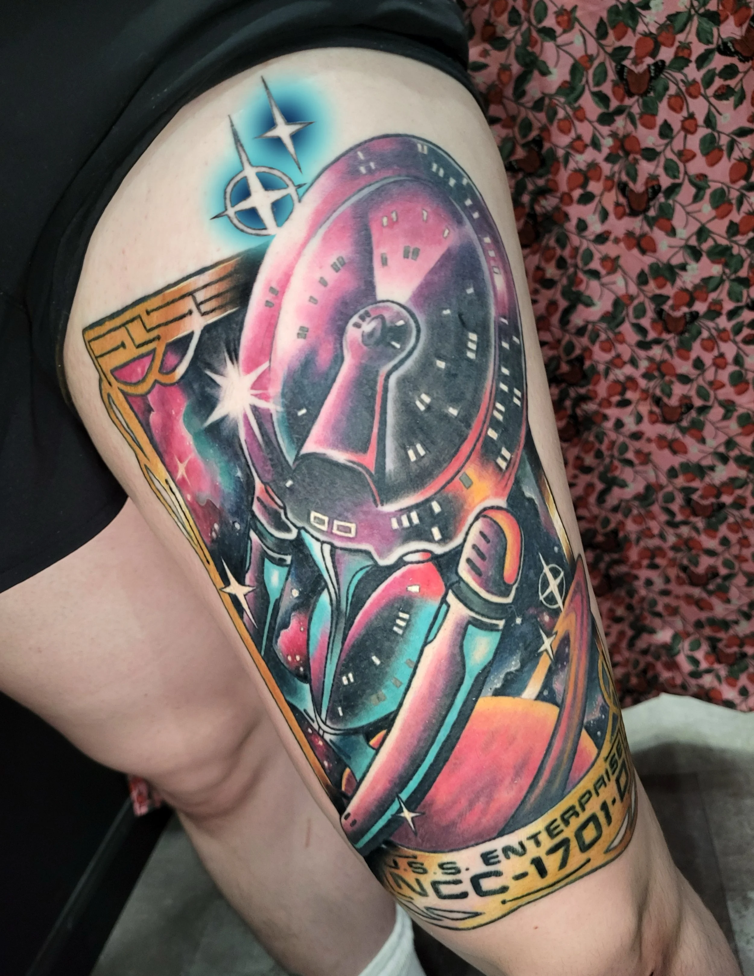 Colorful tattoo of a spaceship or sci-fi scene on a person's upper arm, with stars and cosmic elements visible.
