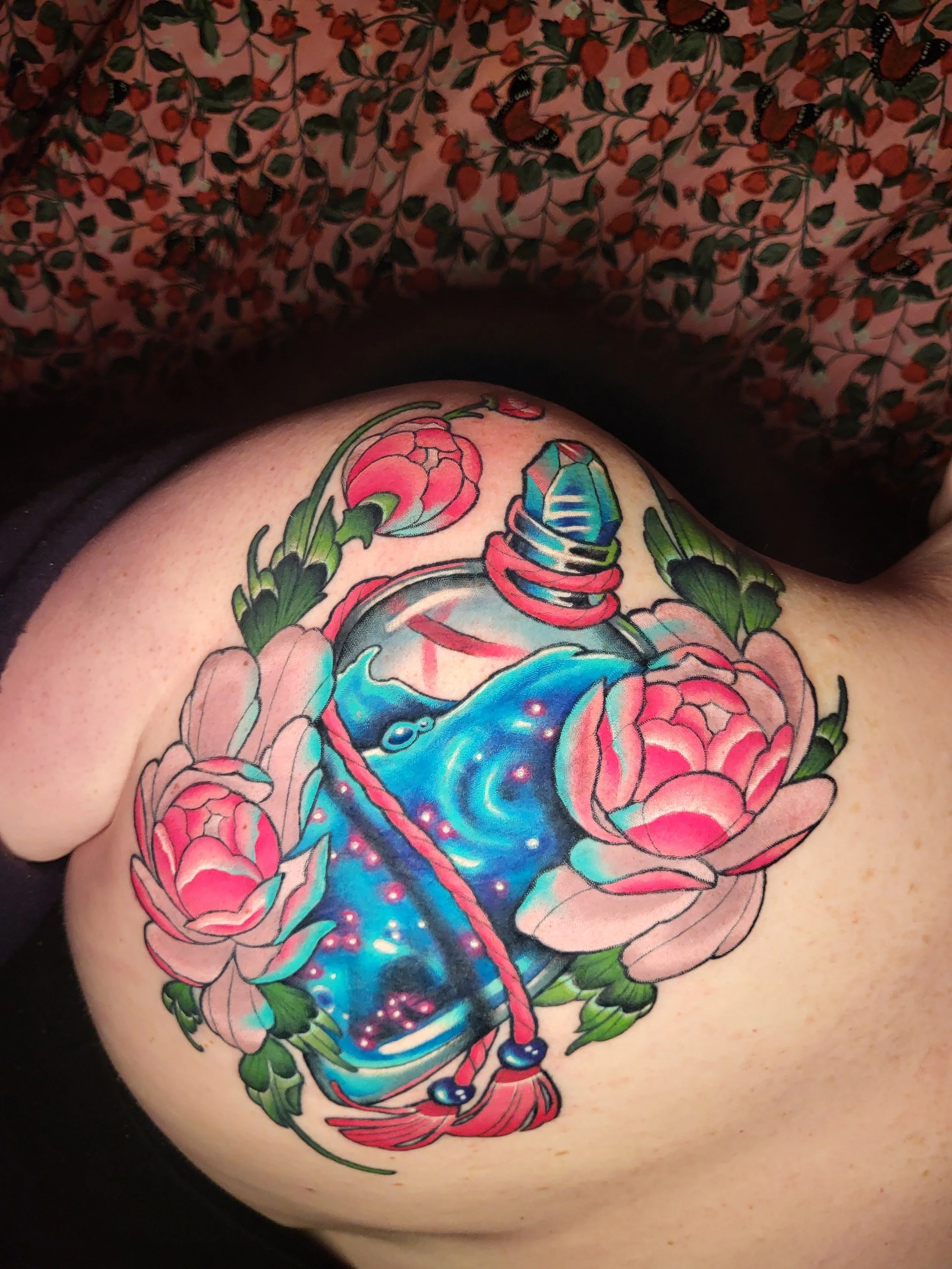 Colorful tattoo of a whale surrounded by pink flowers and green leaves on a person's body.