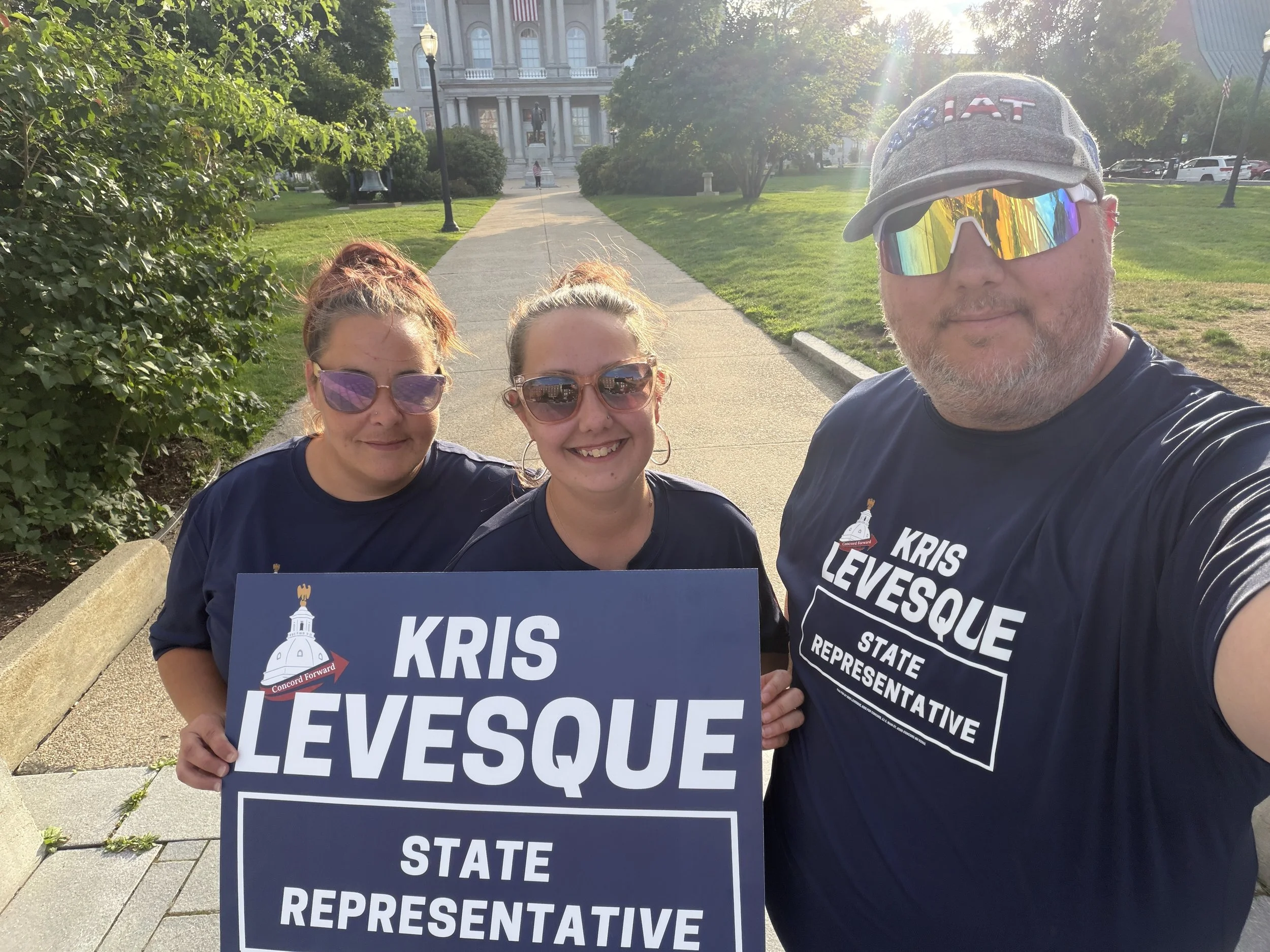 Three supporters in Kris Levesque campaign T-shirts holding a "Kris Levesque, State Representative" yard sign