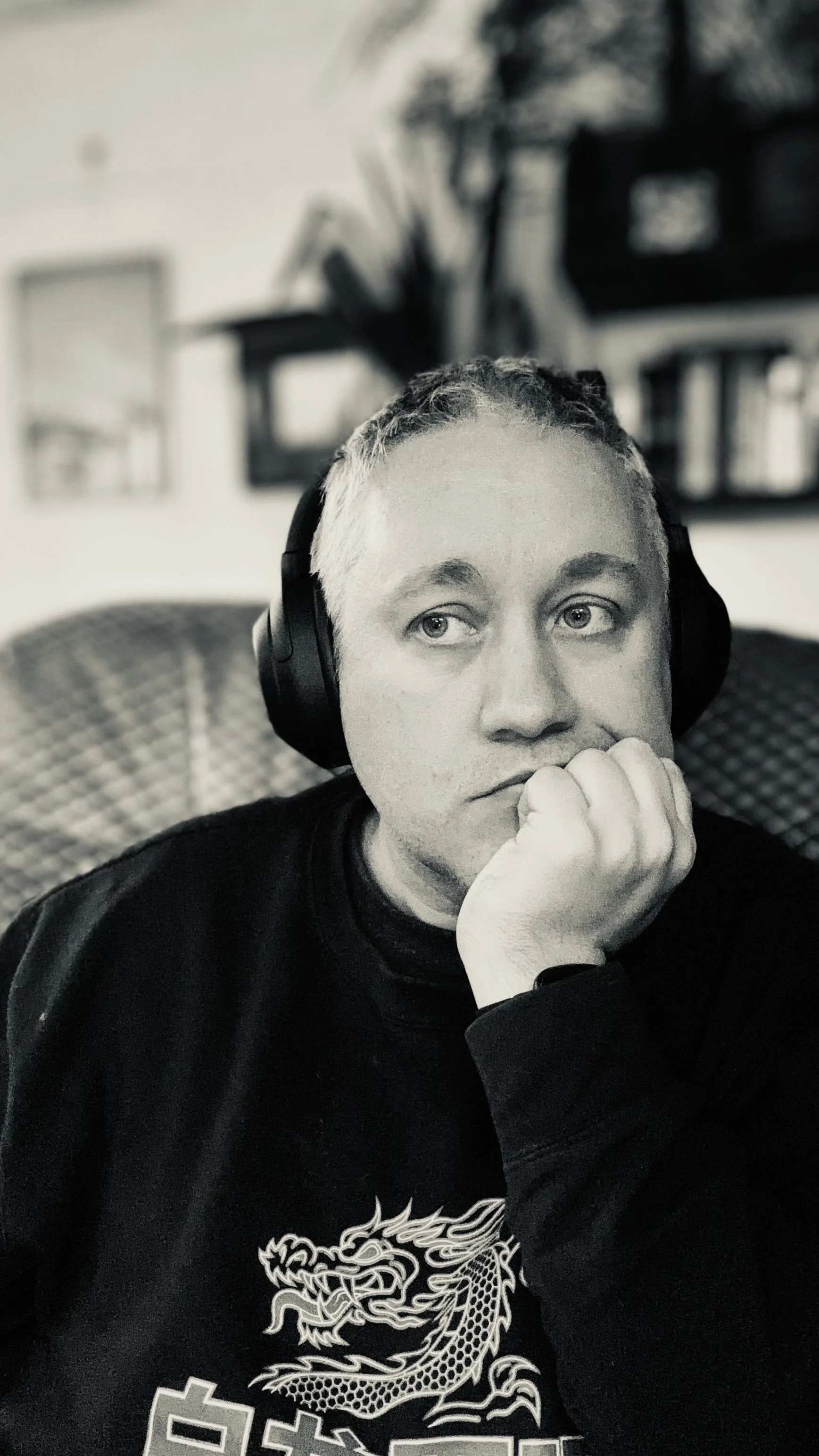 A young man wearing headphones resting his chin on his hand, looking to the side in a black and white photo.