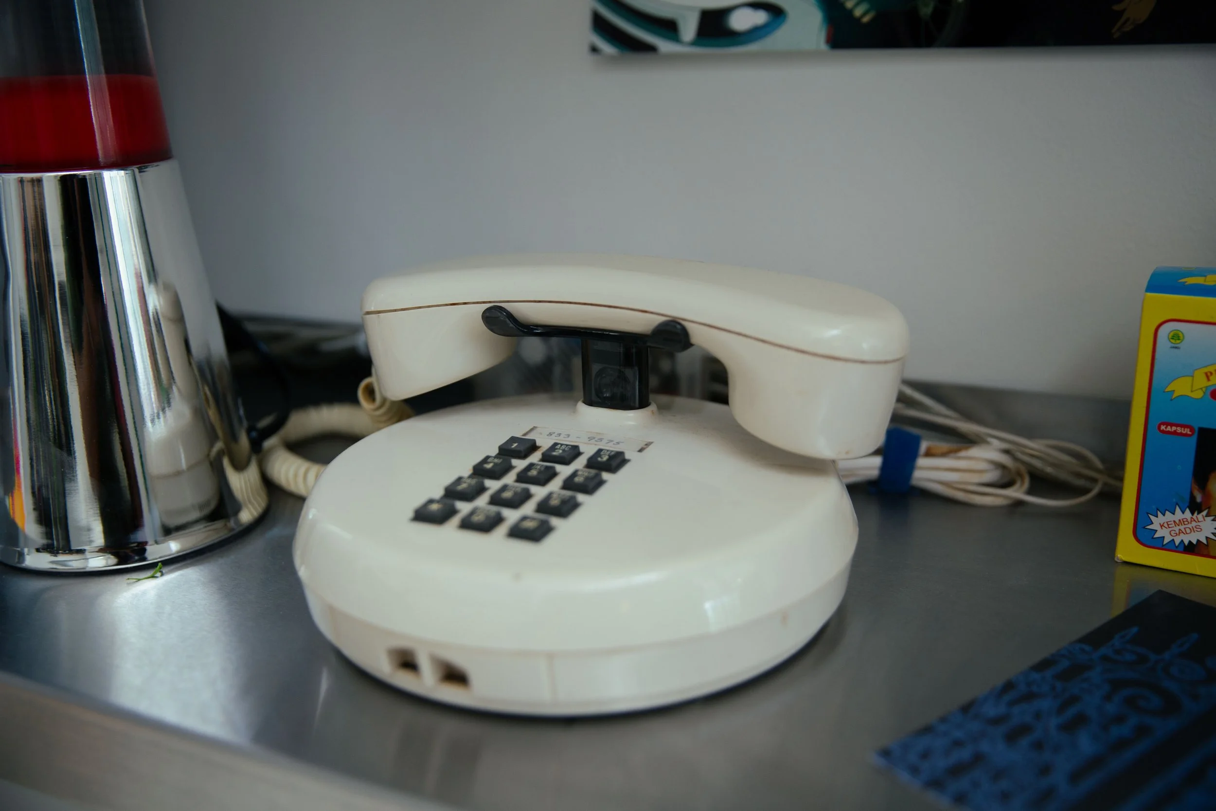 An off-white rotary dial telephone with a cord on a metallic surface.