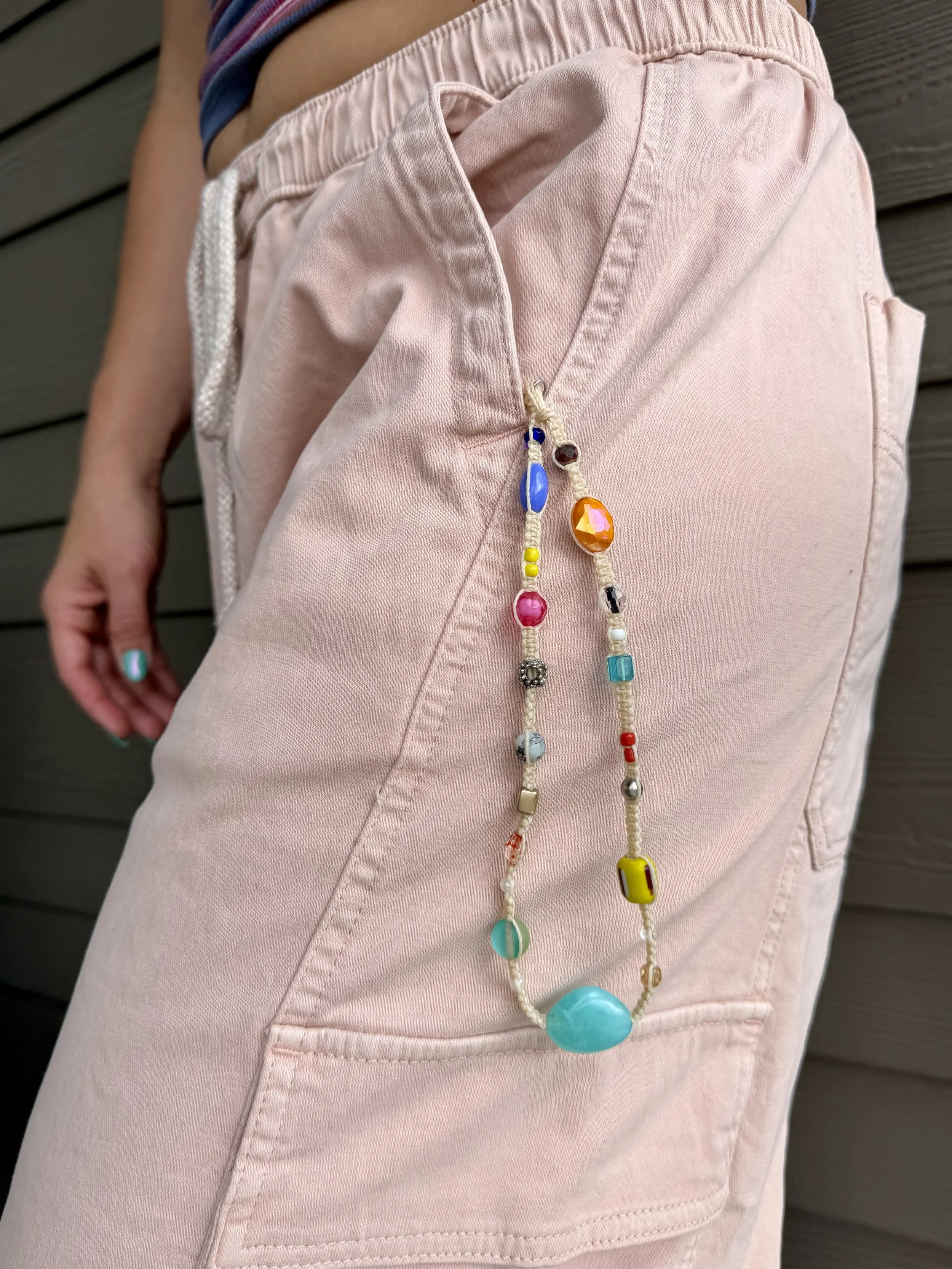 Close-up of a person wearing pink pants with a colorful beaded phone wristlet hanging over the pocket.