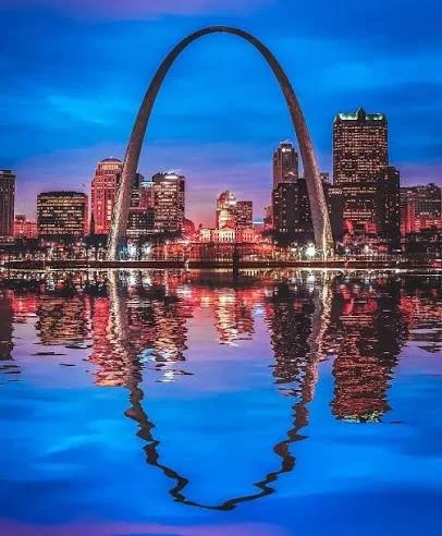 The Gateway Arch towering over the Chicago skyline reflected in the water at dusk.