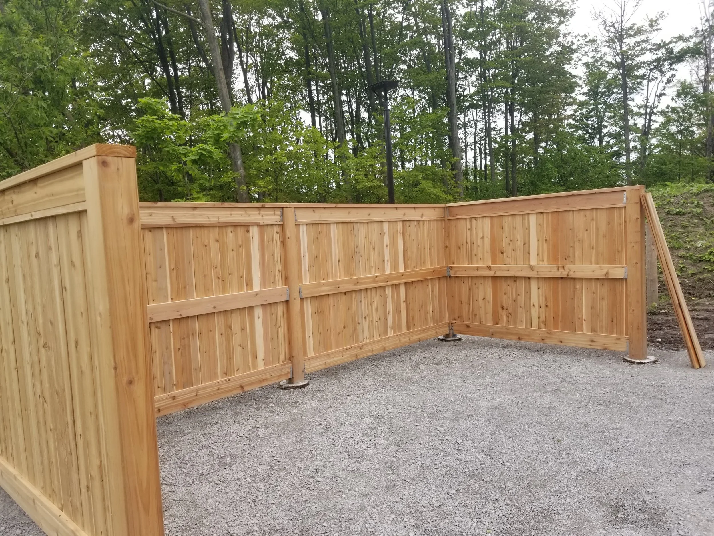 A wooden privacy fence with a corner and a gate, set against a background of trees and forested area with green leaves.