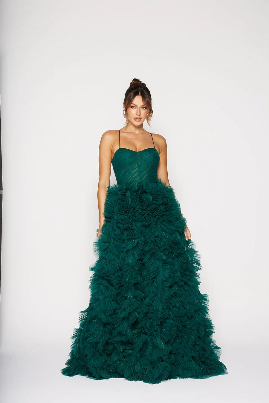 A woman wearing an elegant dark green ball gown with a fitted bodice and a full, ruffled skirt standing against a plain light background.
