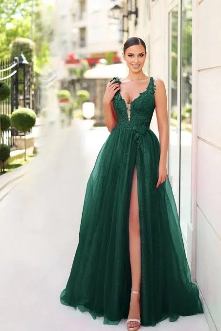 Woman in a long, green, strapless gown with a thigh-high slit, standing outside near a building, holding a small clutch purse.