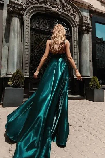 Woman in a long, teal satin gown standing in front of an ornate black iron gate outside a building.