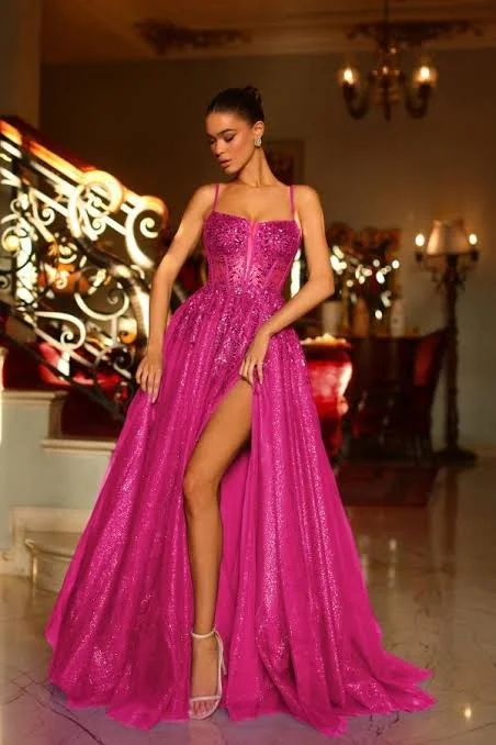 Woman in a pink, sparkly evening gown with a high slit, standing in an elegant interior with a staircase and chandeliers.