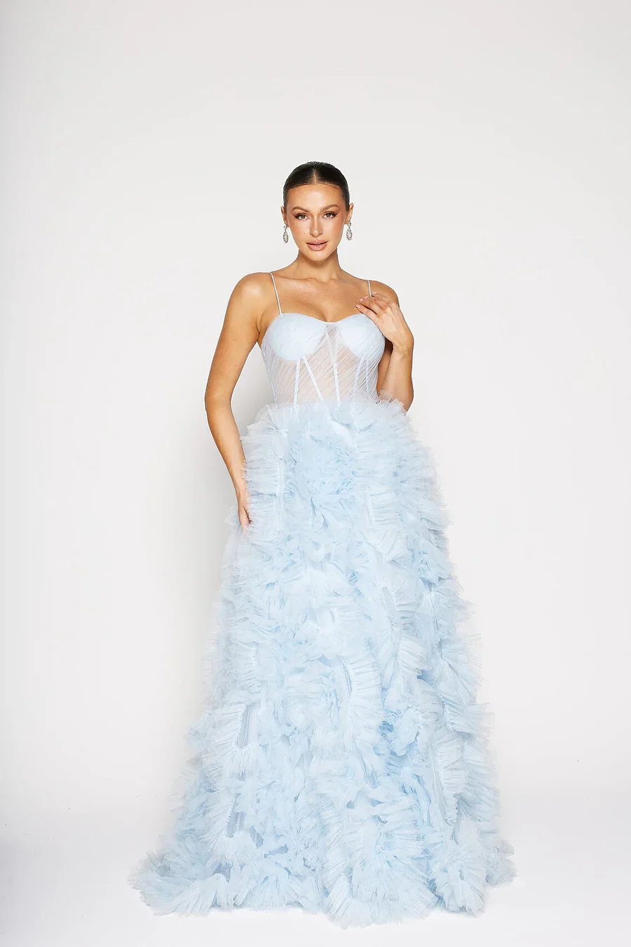 A woman in a white wedding gown with a fitted bodice and a voluminous, textured skirt stands against a plain white background.