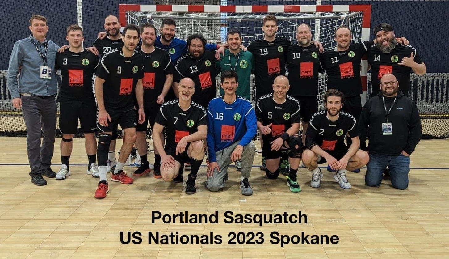 A team of 14 men wearing black sports jerseys with green logos and red sponsorship logos, posing on an indoor sports court in front of a goal net. Some are kneeling, others standing. The caption states they are Portland Sasquatch, US Nationals 2023 Spokane.