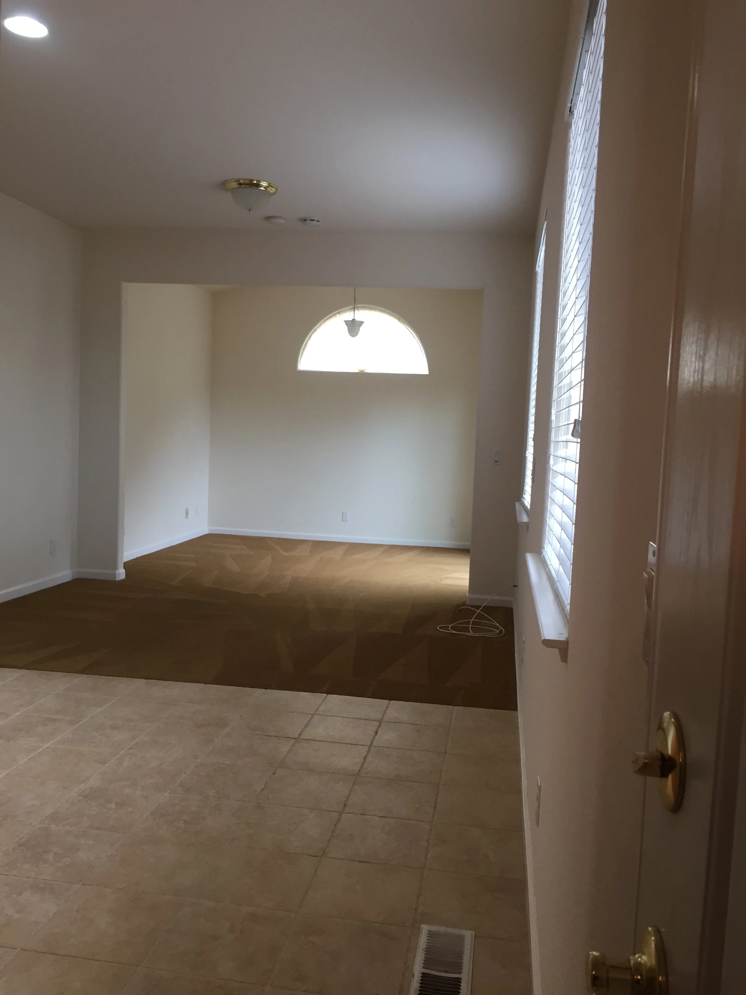 Empty room with hardwood flooring, beige walls, and a window with blinds, seen from the doorway.
