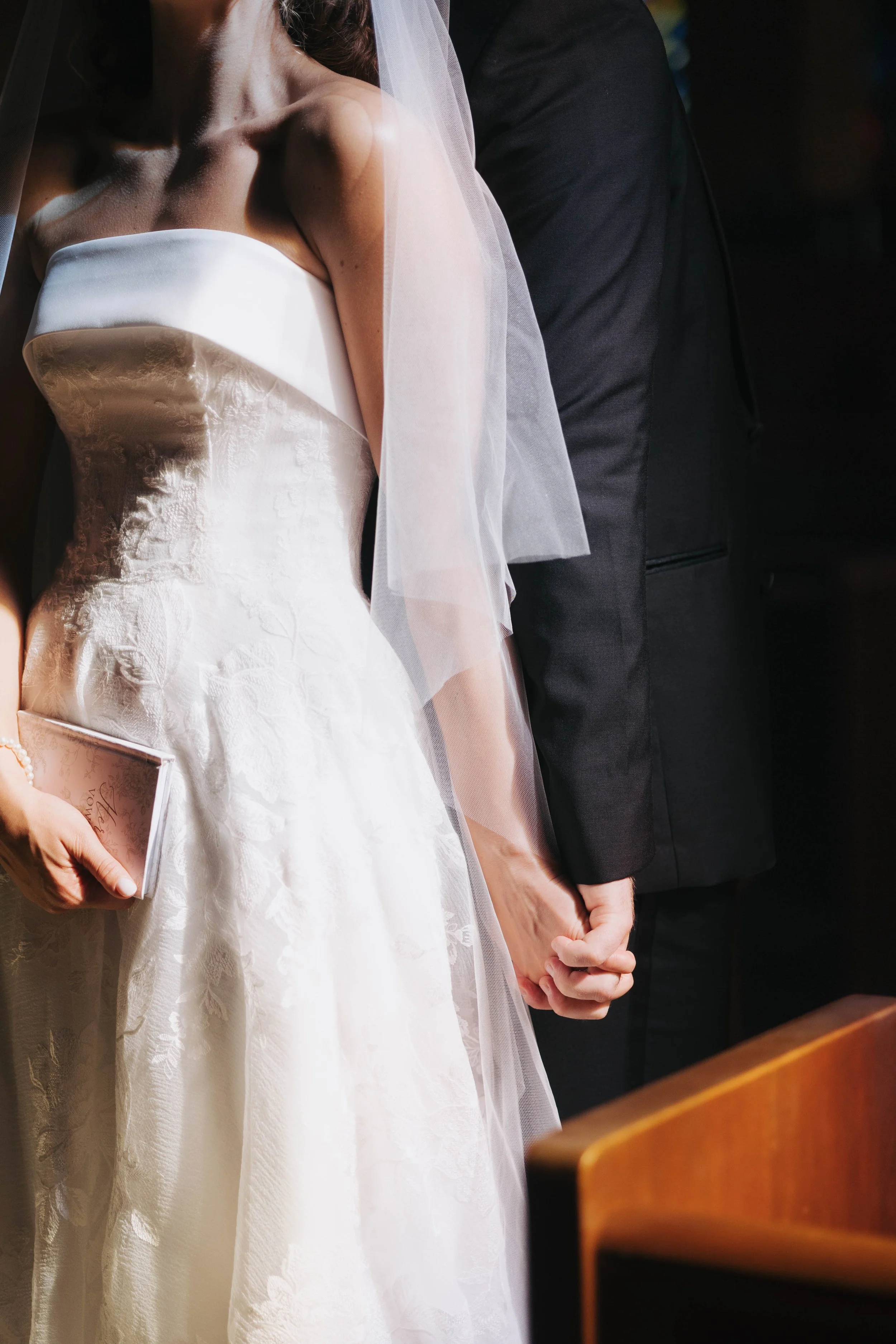 Close-up of a bride and groom holding hands during their private vows before their wedding ceremony, the bride wearing a white wedding dress and veil, and the groom dressed in a black suit.