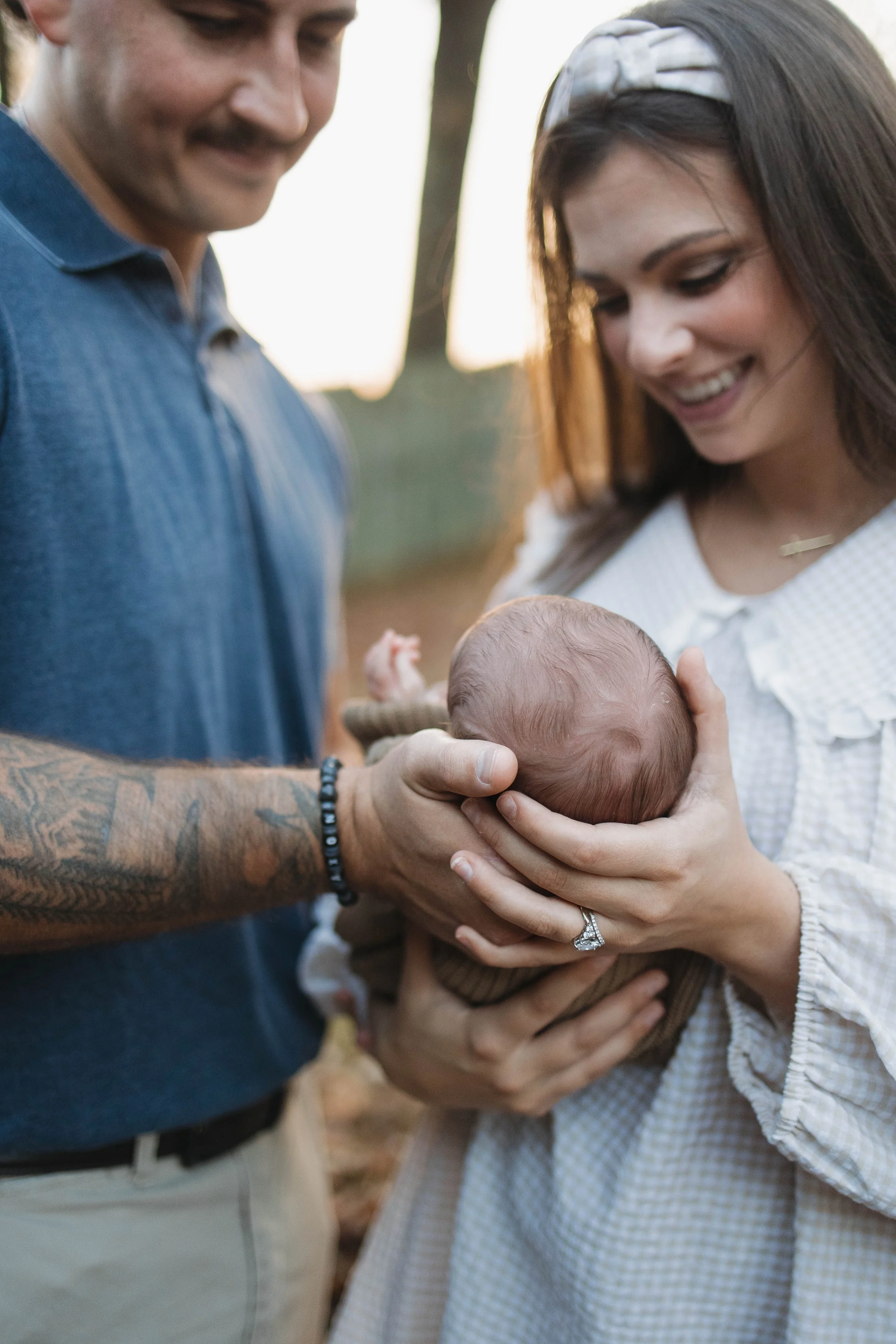 A man and woman holding a newborn baby outdoors during sunset.