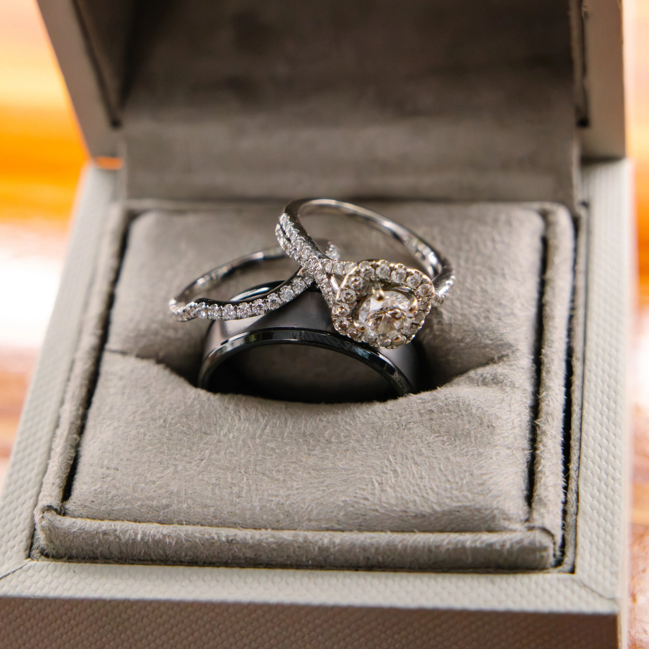 Close-up of a jewelry box containing a diamond ring with multiple gemstones, set inside a gray cushioned interior.