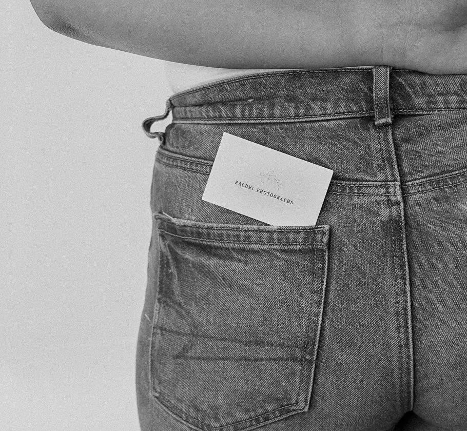 Close-up of a person wearing jeans with a business card in the back pocket that reads "Rachel Photographs".