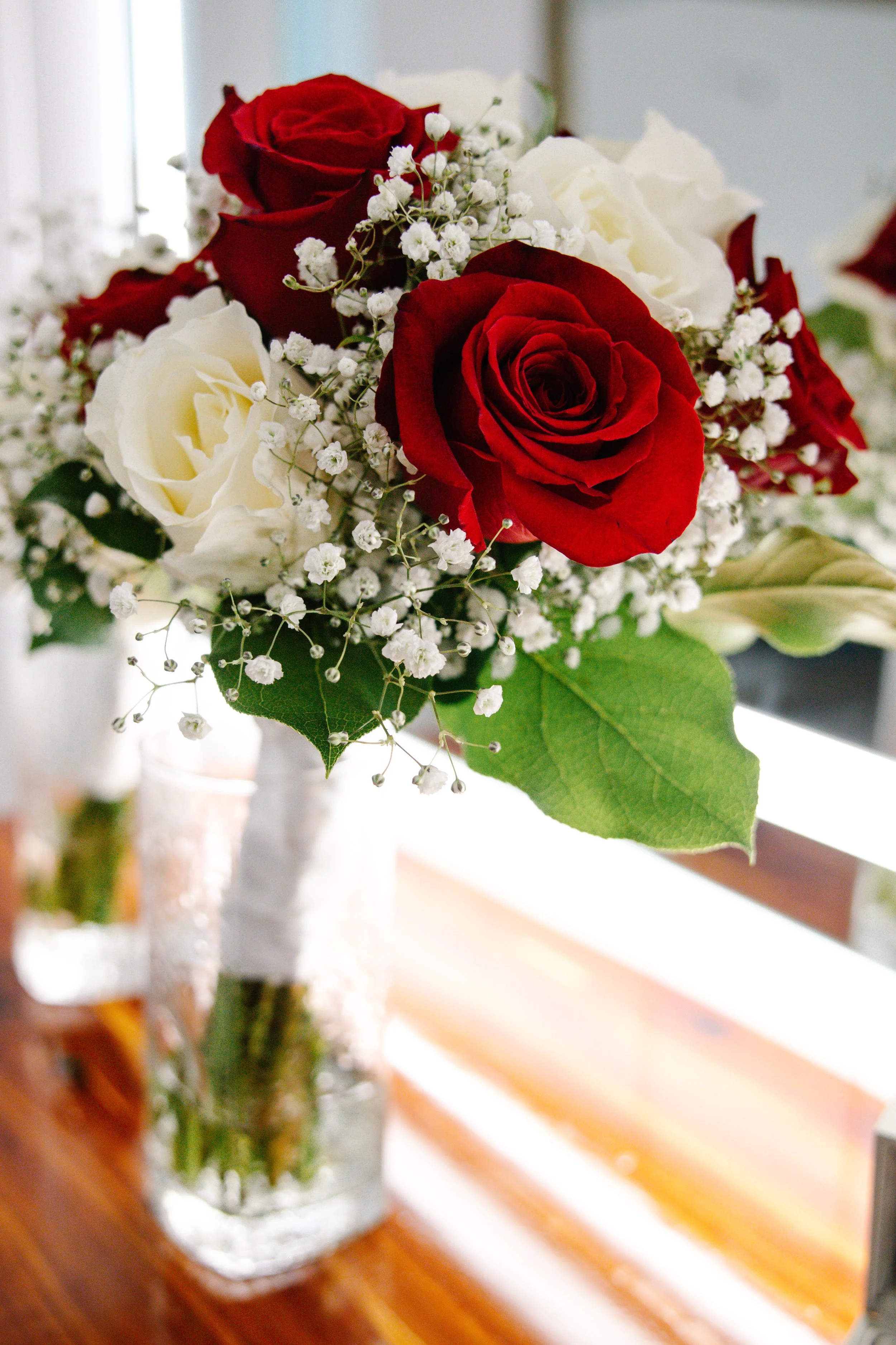 A bouquet of red and white roses with baby's breath in a glass vase on a wooden table.