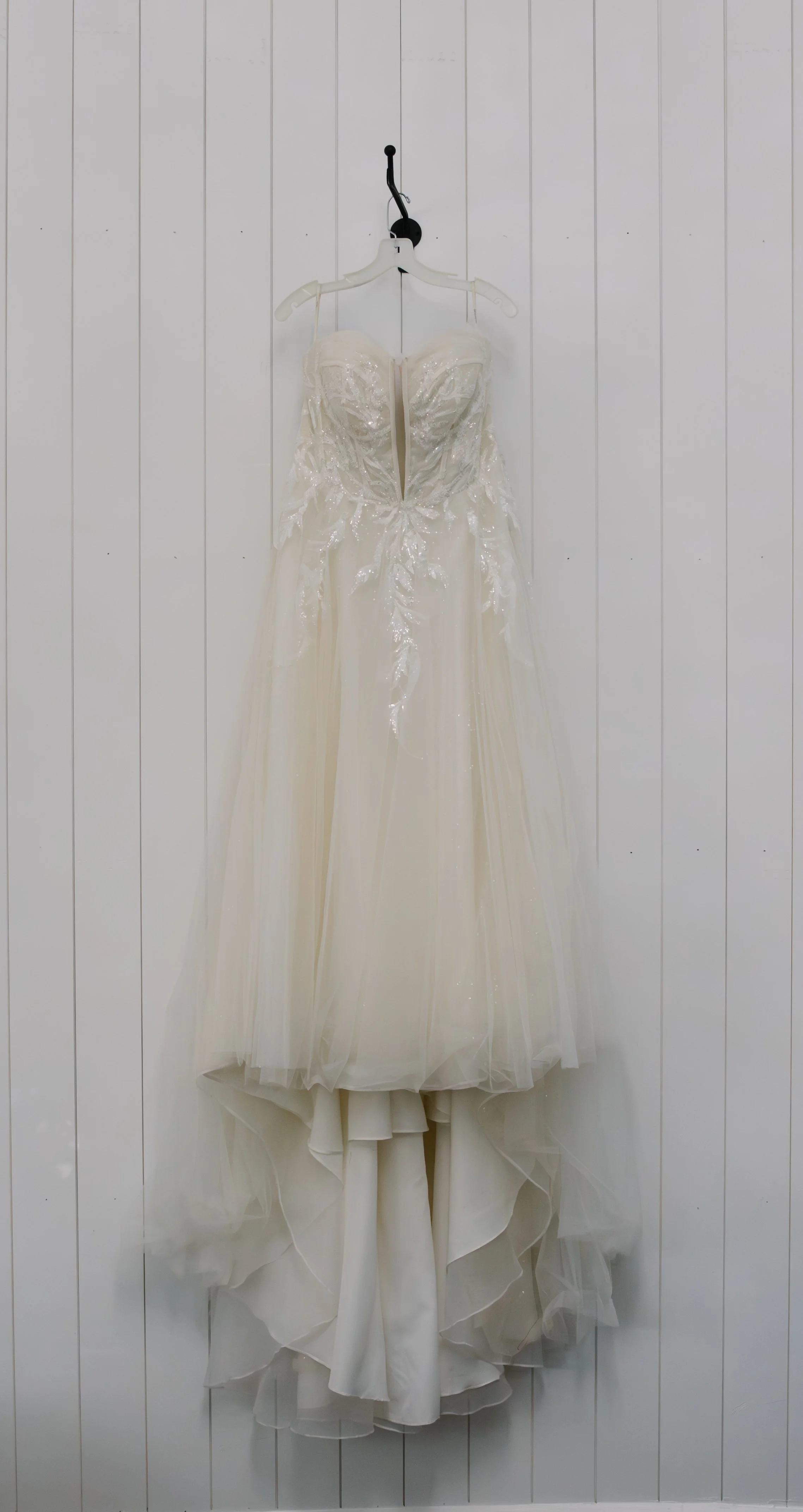 White wedding dress hanging on a wall with white paneling.