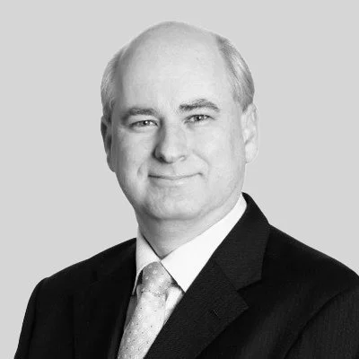 Black and white professional portrait of a middle-aged man wearing a suit and tie, smiling slightly.