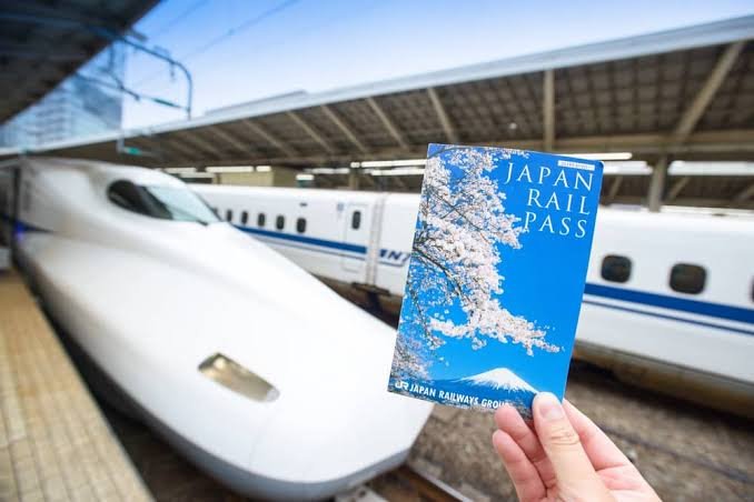 Person holding a Japan Rail Pass in front of a bullet train at a train station.