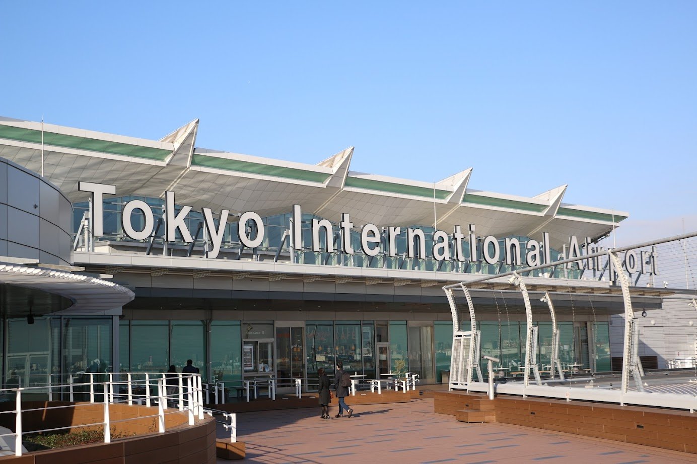 Exterior view of Tokyo International Airport building with people walking outside, clear sky.