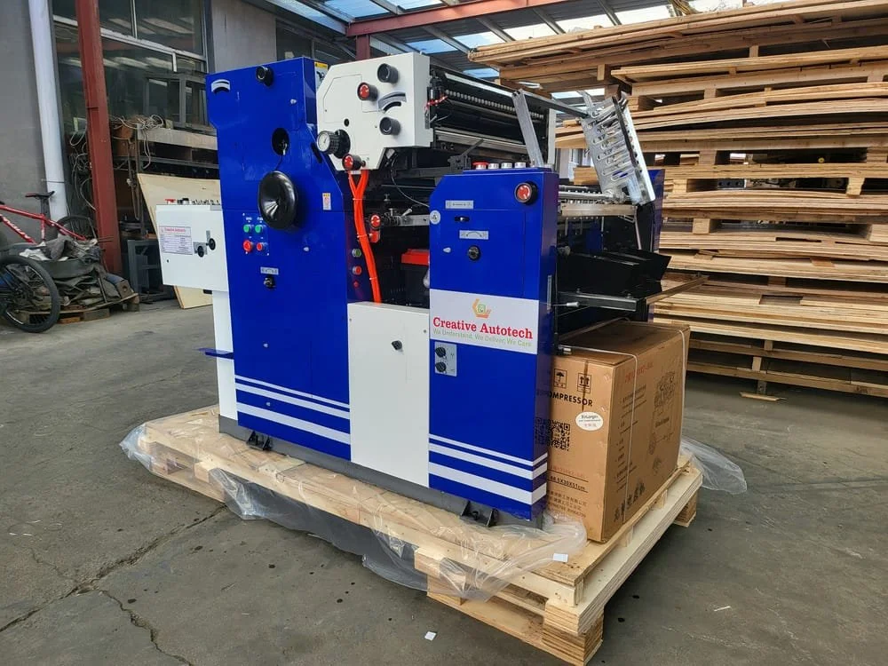 Industrial machine on a wooden pallet in a warehouse, with a cardboard box and wooden shelves in the background.