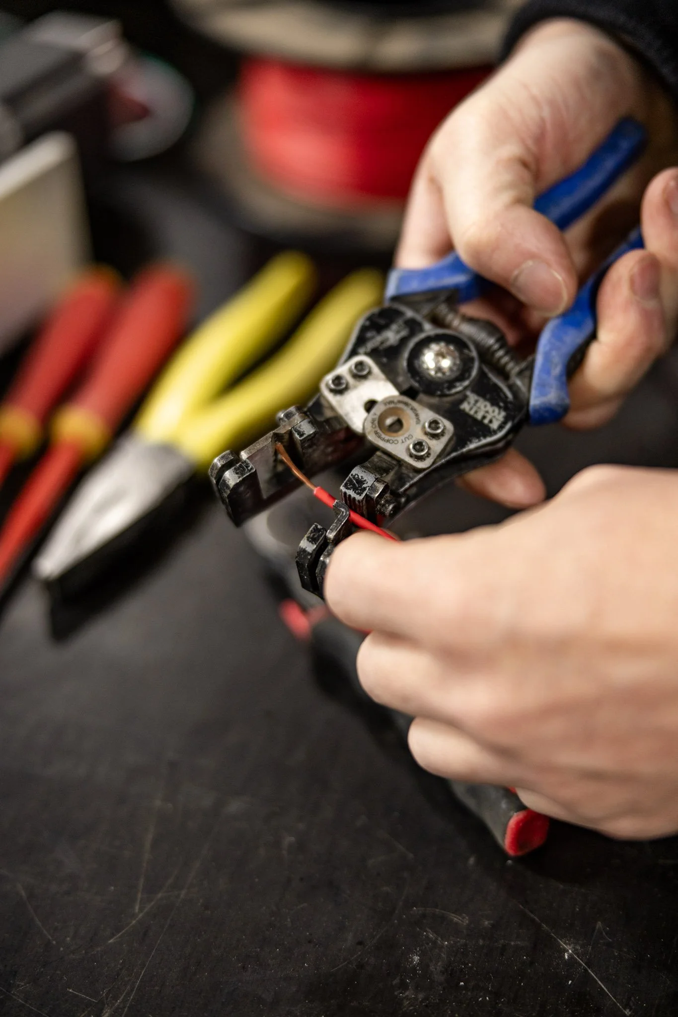 Close-up of a person using wire cutters to cut a red wire, with various colored wires in the background.