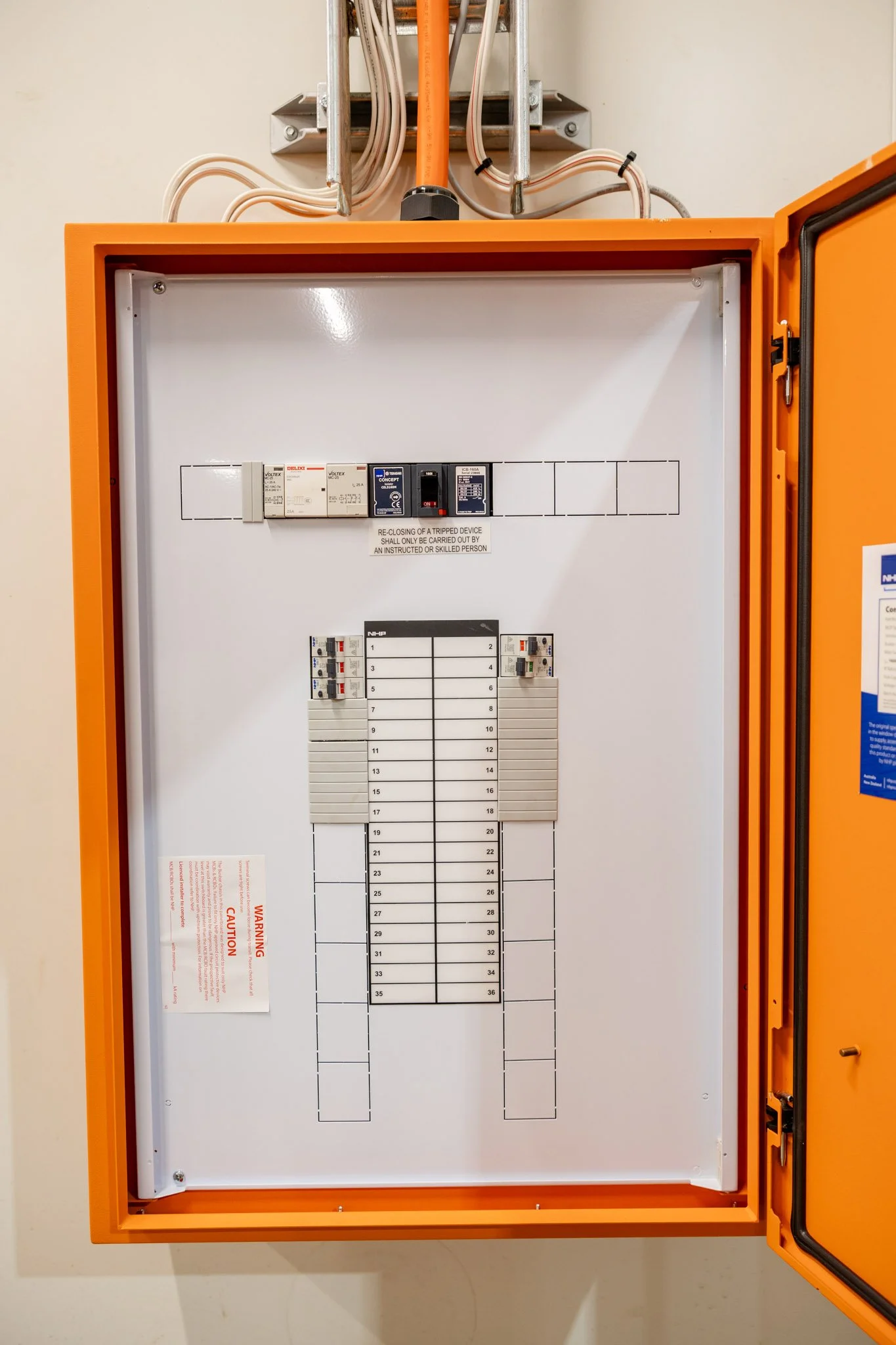 An electrical control panel with circuit breakers and a wiring diagram inside an orange metal box.