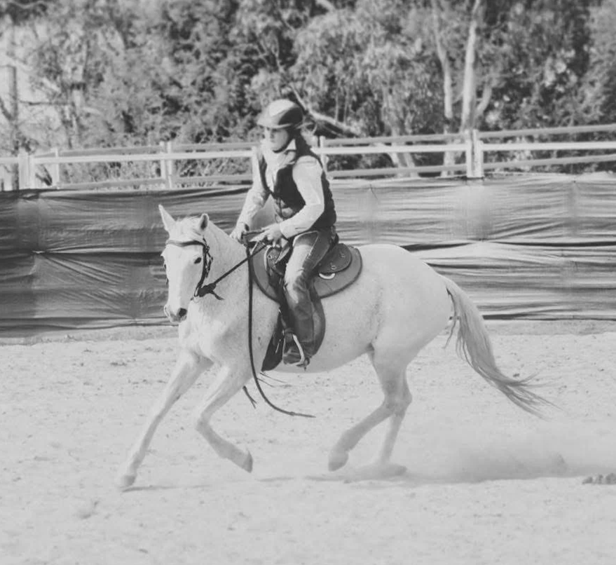 A person riding a white horse during a riding session in an outdoor arena.