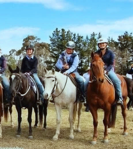 Four people riding horses in an outdoor setting with trees in the background.