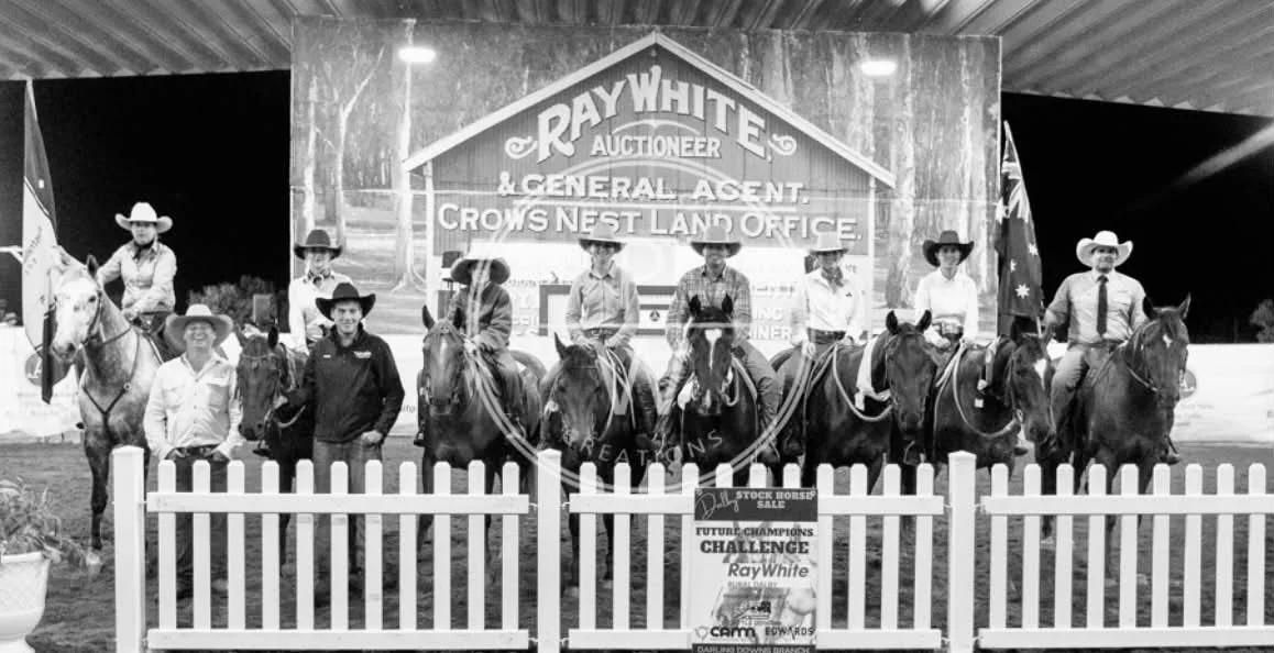 Group of people on horseback and standing in front of a large sign that reads 'Ray White Auctioneer & General Agent Crows Nest Land Office' at a rodeo or equestrian event.