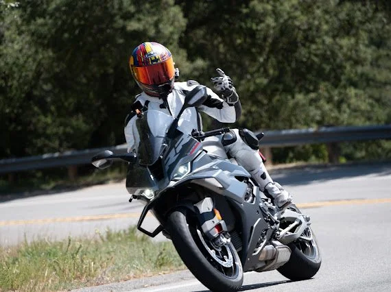Motorcyclist wearing a helmet and riding a gray motorcycle on a curved road.