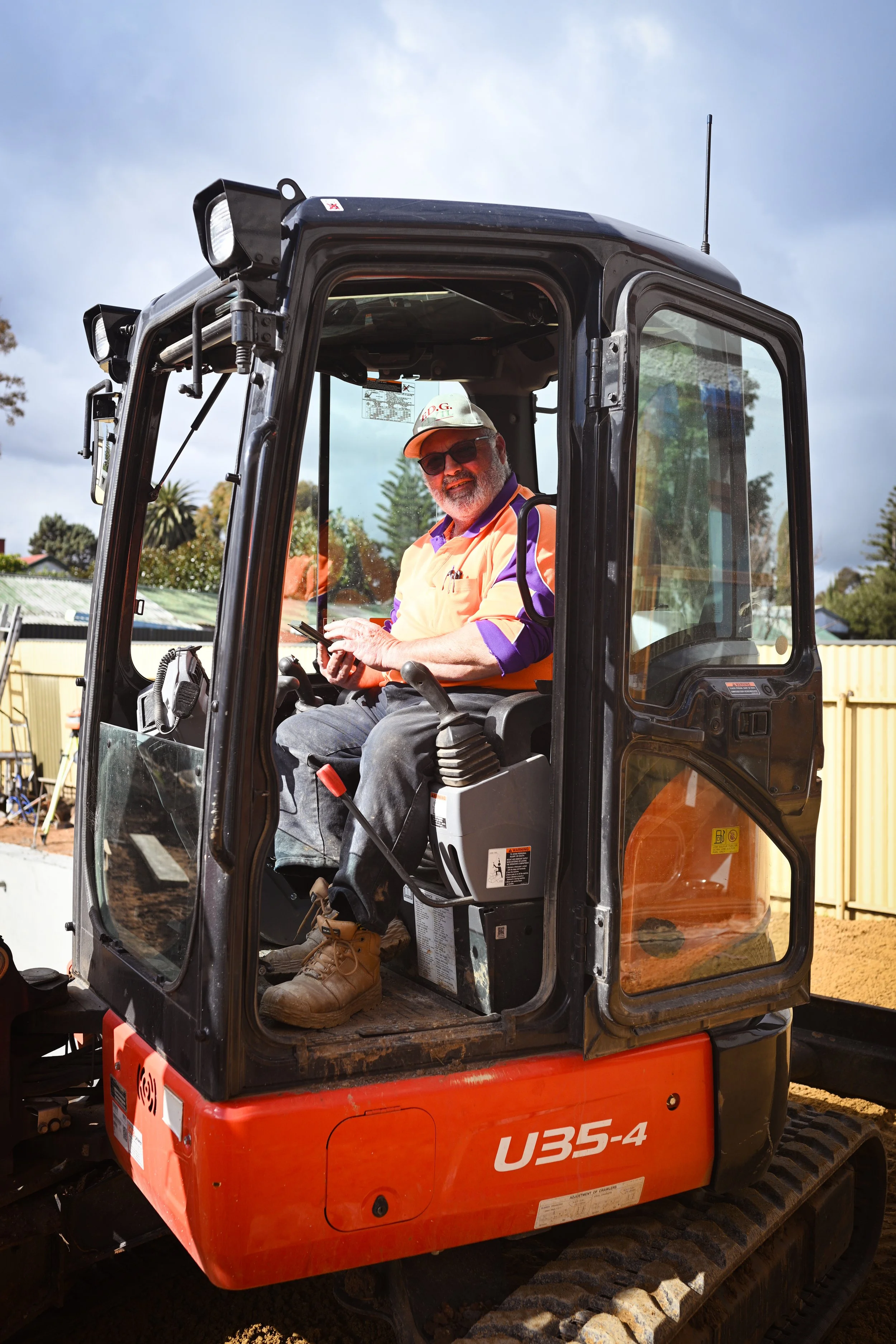 A man with sunglasses and a cap sitting in an orange and black U35-4 compact excavator, operating it at a construction site during daytime.