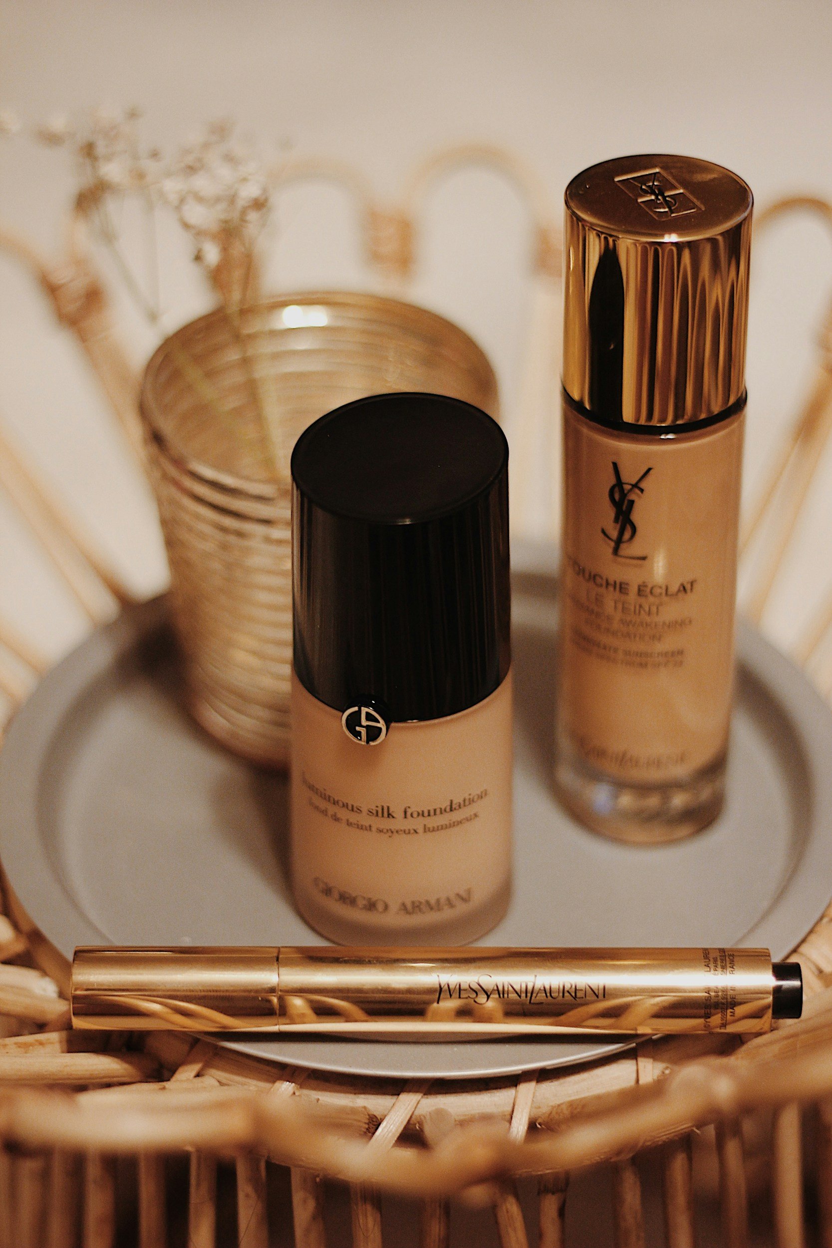 Beauty products including Yves Saint Laurent Foundation, Dior foundation, and YSL lip primer placed on a woven basket.