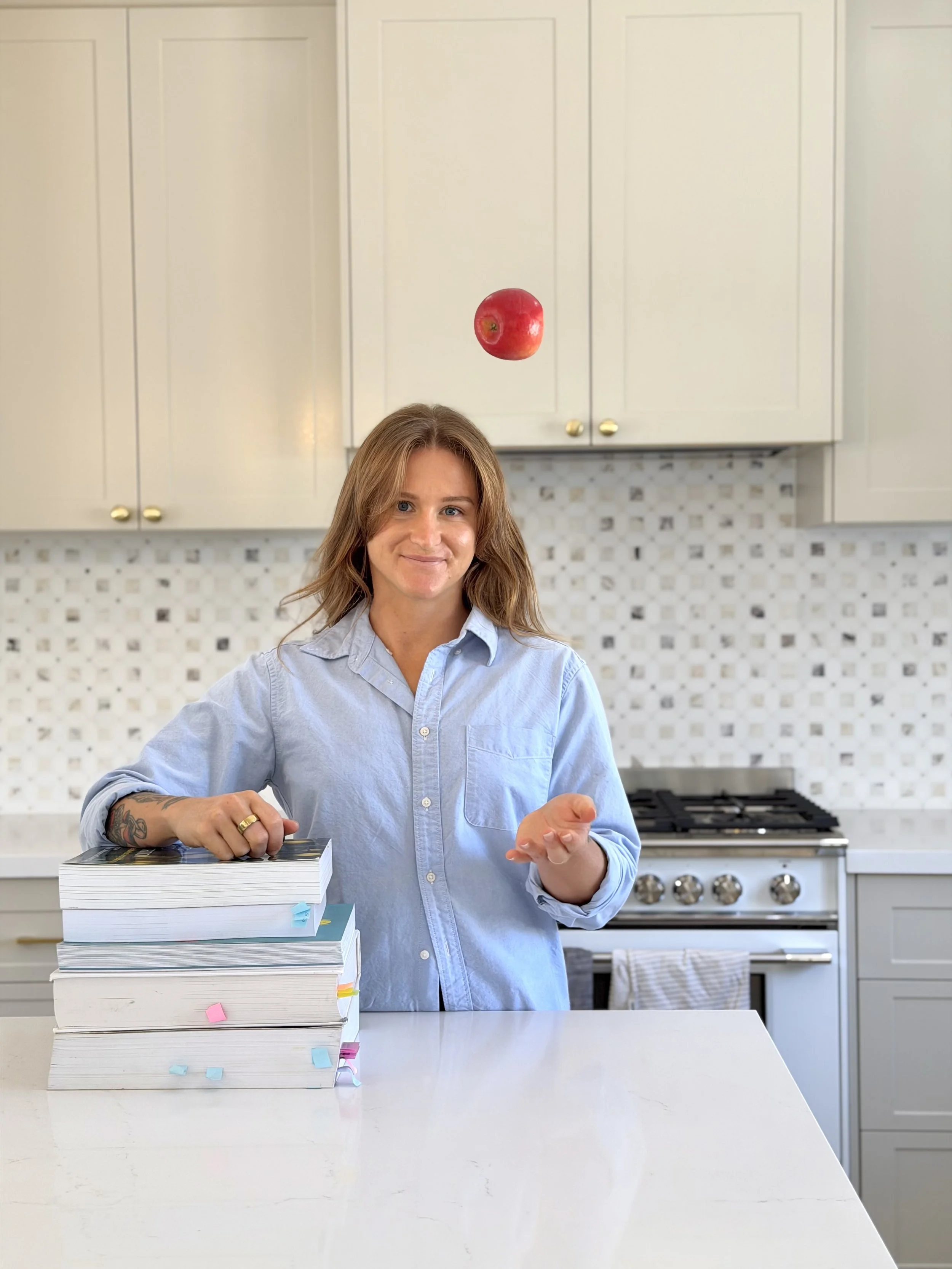 Jana Zak-Clinical-Nutritonist-Mandurah-Perth-Peel-Region-In her kitchen in falcon throwing an apple in the air with books
