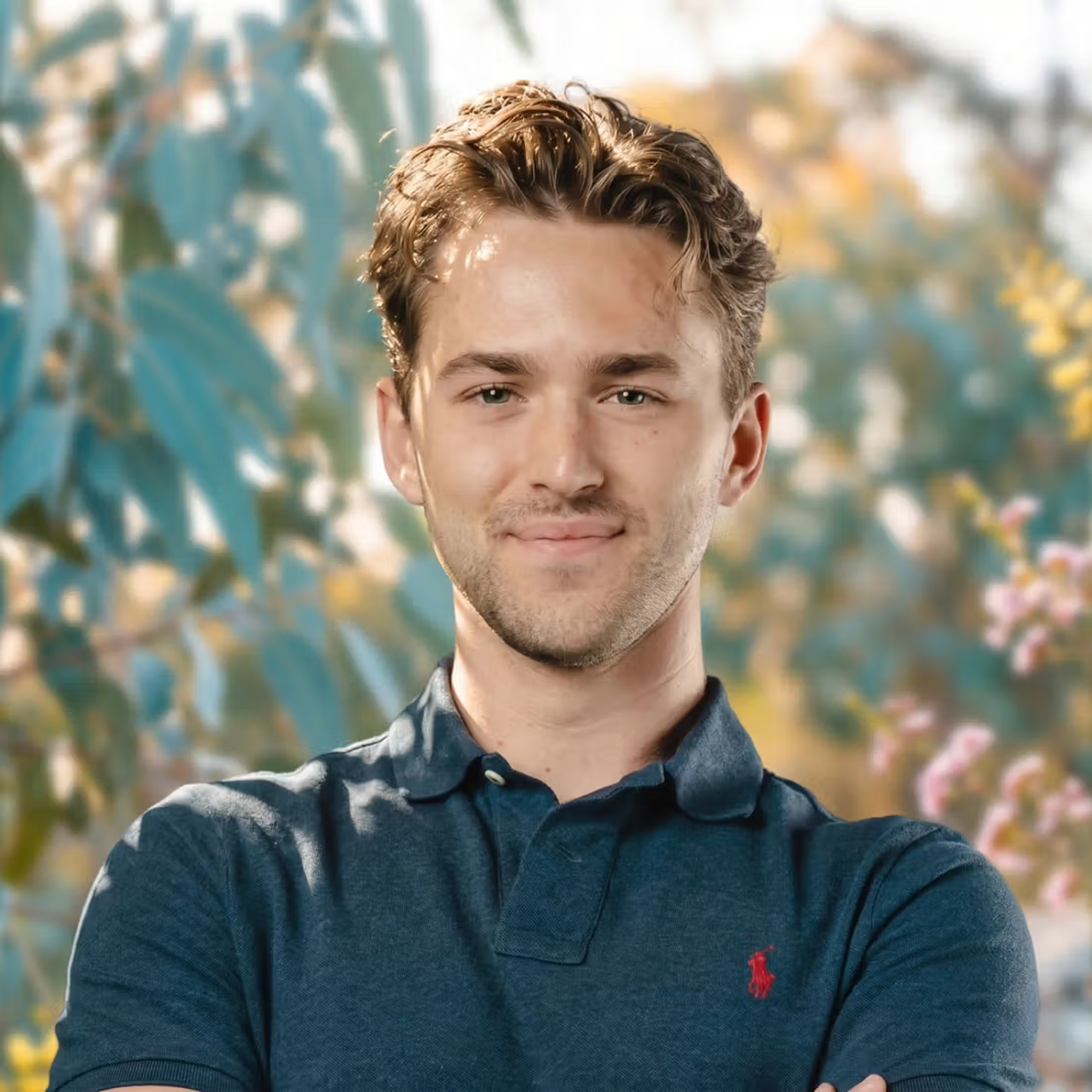 Close-up of Hayden Green, smiling, outdoors with blurred trees and plants in the background.