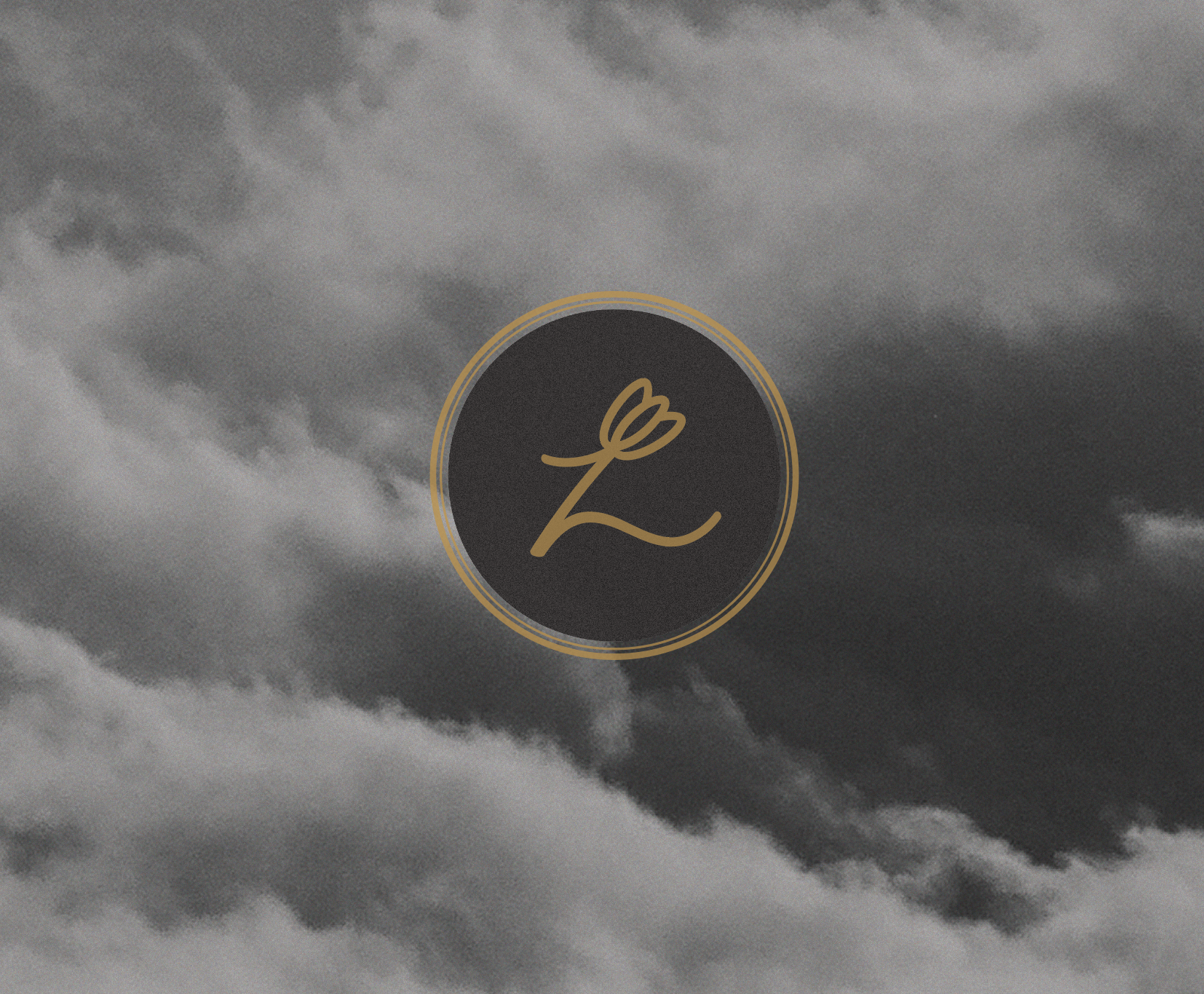 A dark, cloudy sky with a black circular logo in the center outlined with gold. The logo features a gold, stylized letter 'L' with a small floral element at the top.