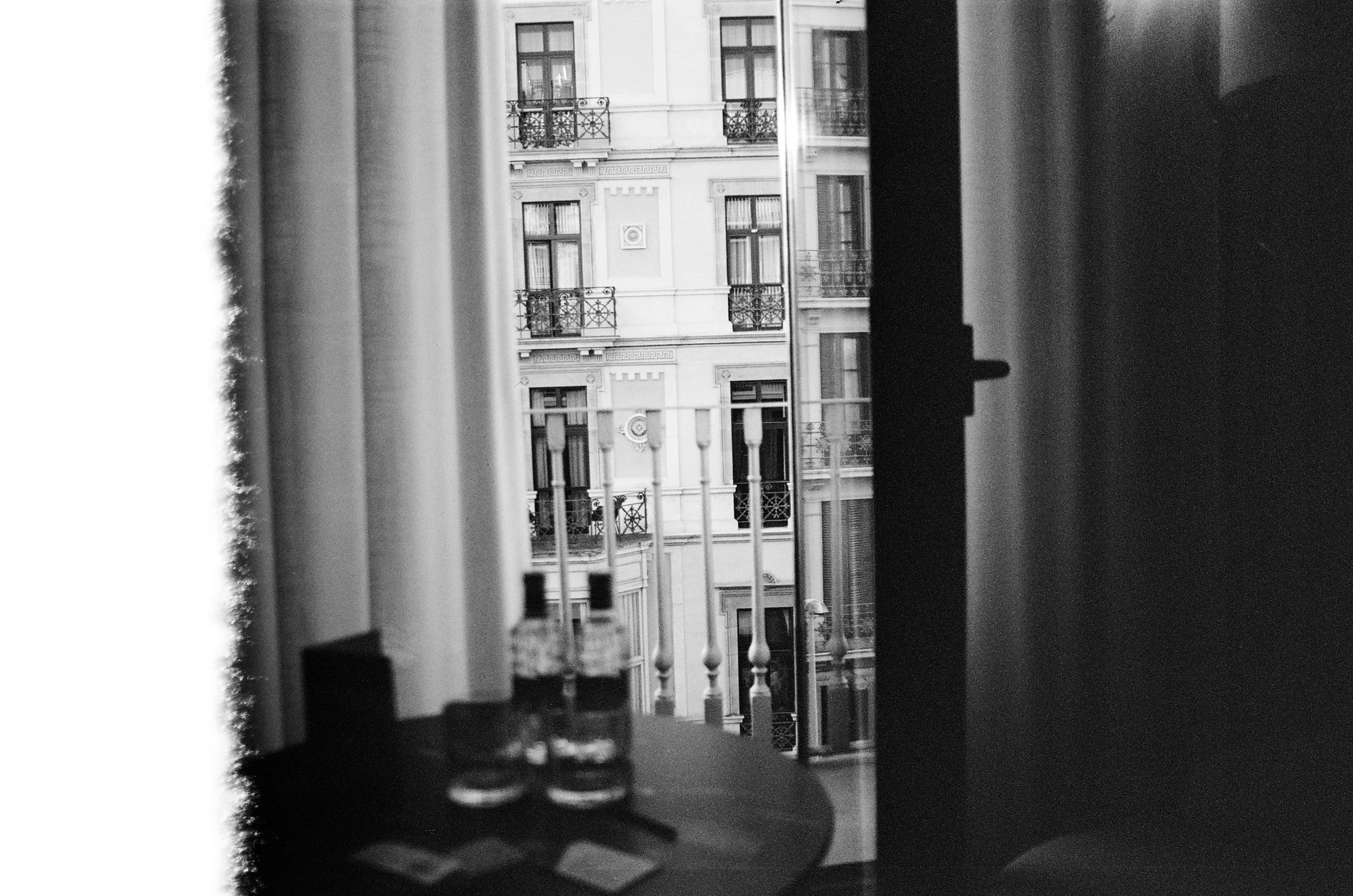 View of European-style apartment building with balconies through a window with curtains, black and white photograph.