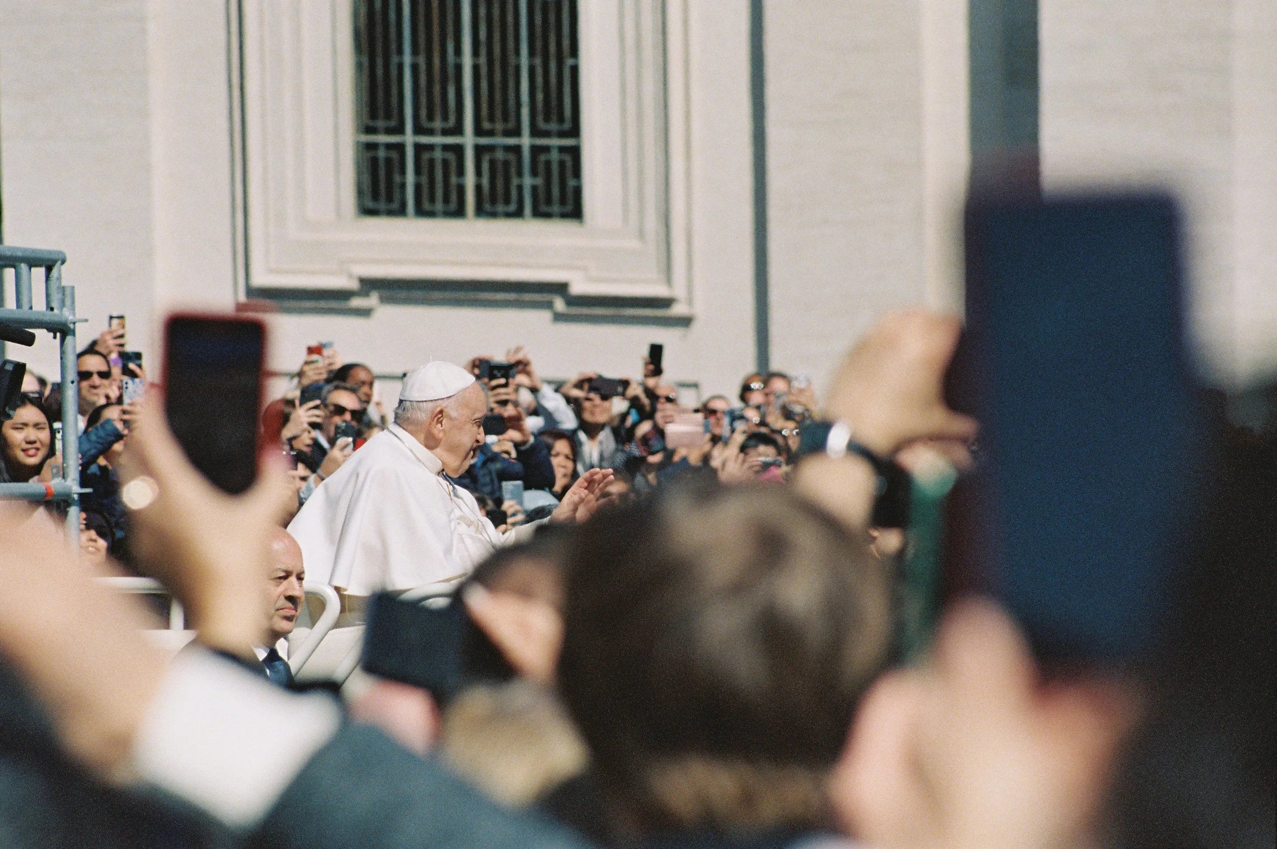 A crowd of people taking photos and videos of a man dressed in white, likely at a public event or outdoor gathering.