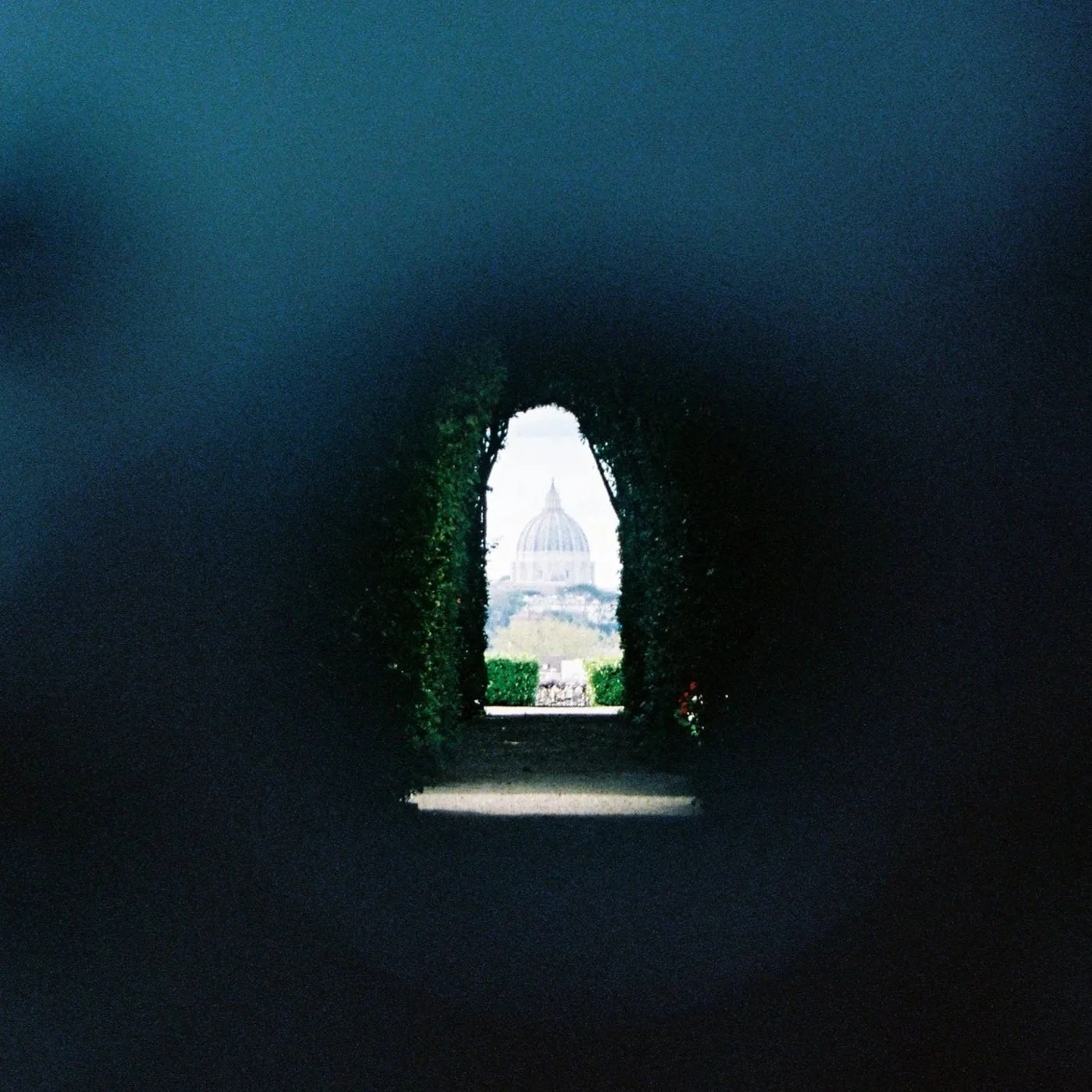 View of a dome-shaped building seen through a dark, arched opening in greenery.