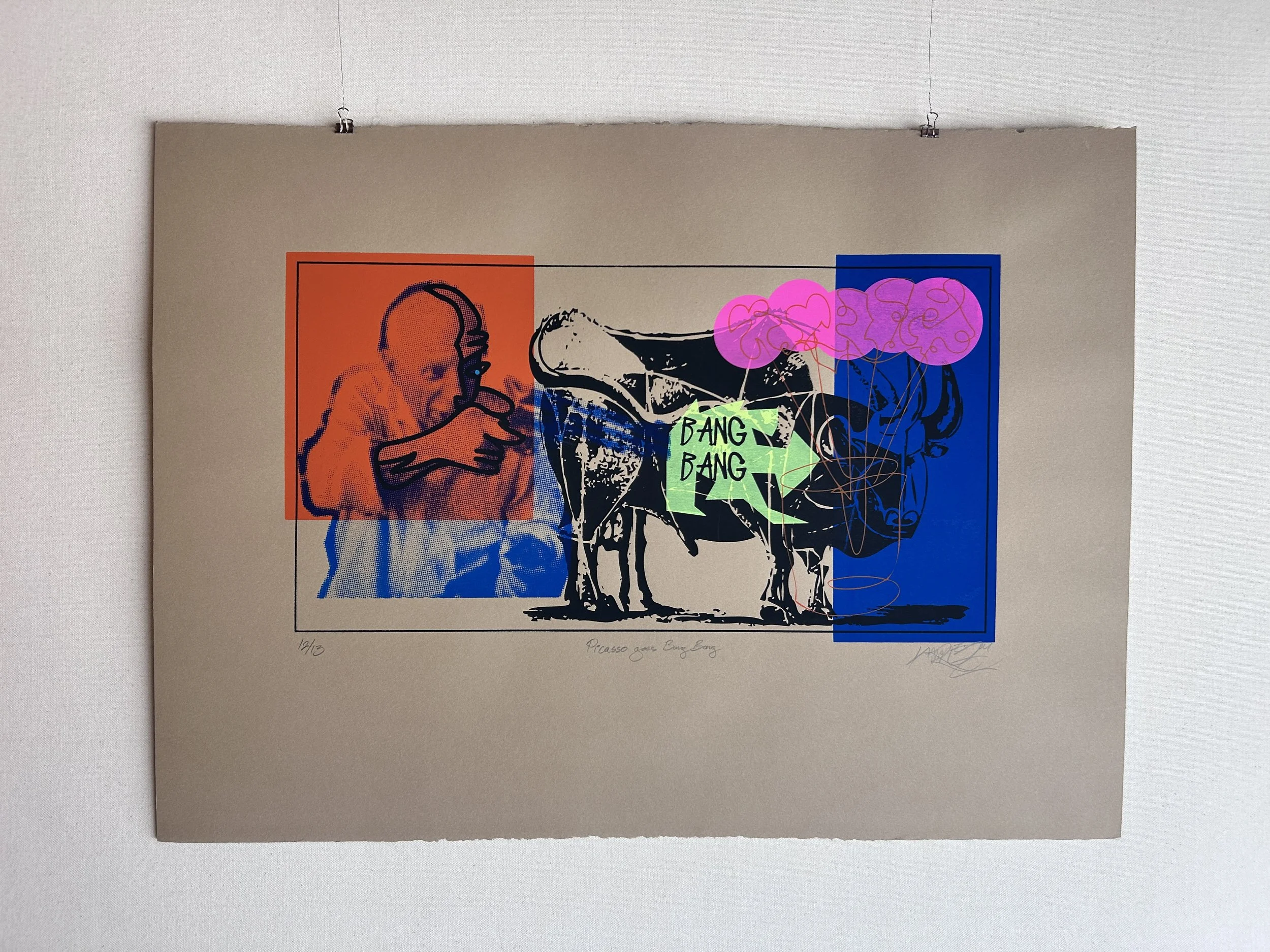 A colorful artwork featuring a stylized portrait of a man with headphones on left, a black and white line drawing of a dog or bull in the center, and abstract pink and purple cloud-like shapes on the right. The artwork has a beige background and is titled "Picasso goes Bang Bang" with edition number "12/13" and artist's signature.