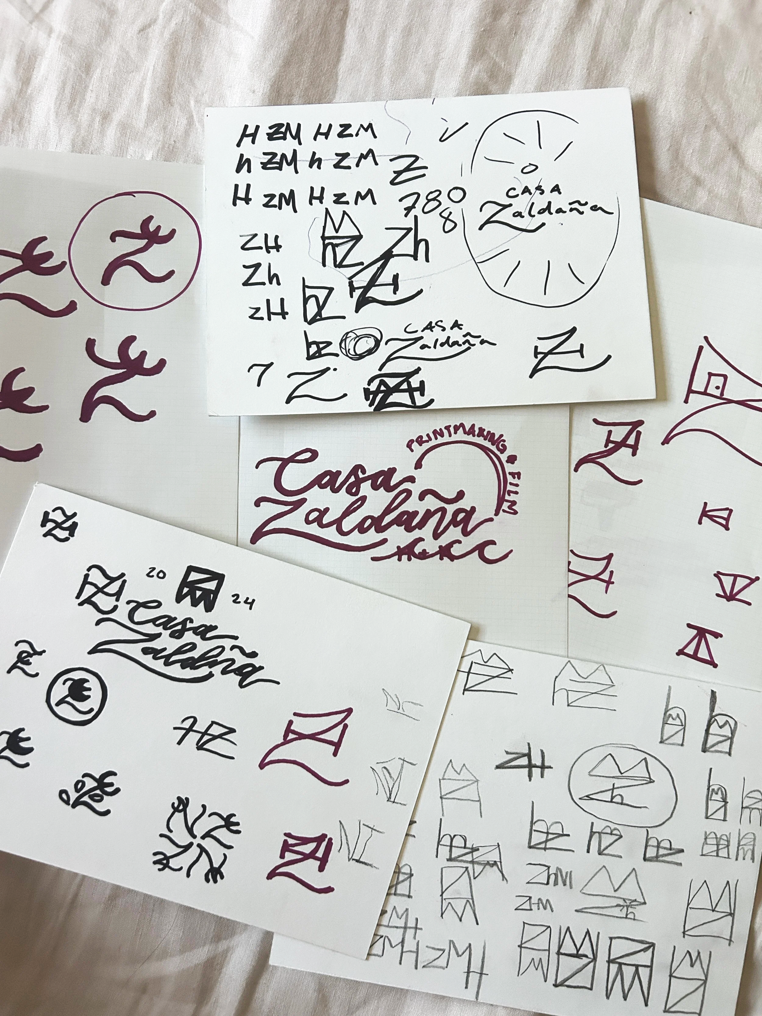 Several sheets of paper contain handwritten sketches, symbols, and the text 'Casa Zaldana' written in stylized font. Some notes include various shapes, lines, and annotations.