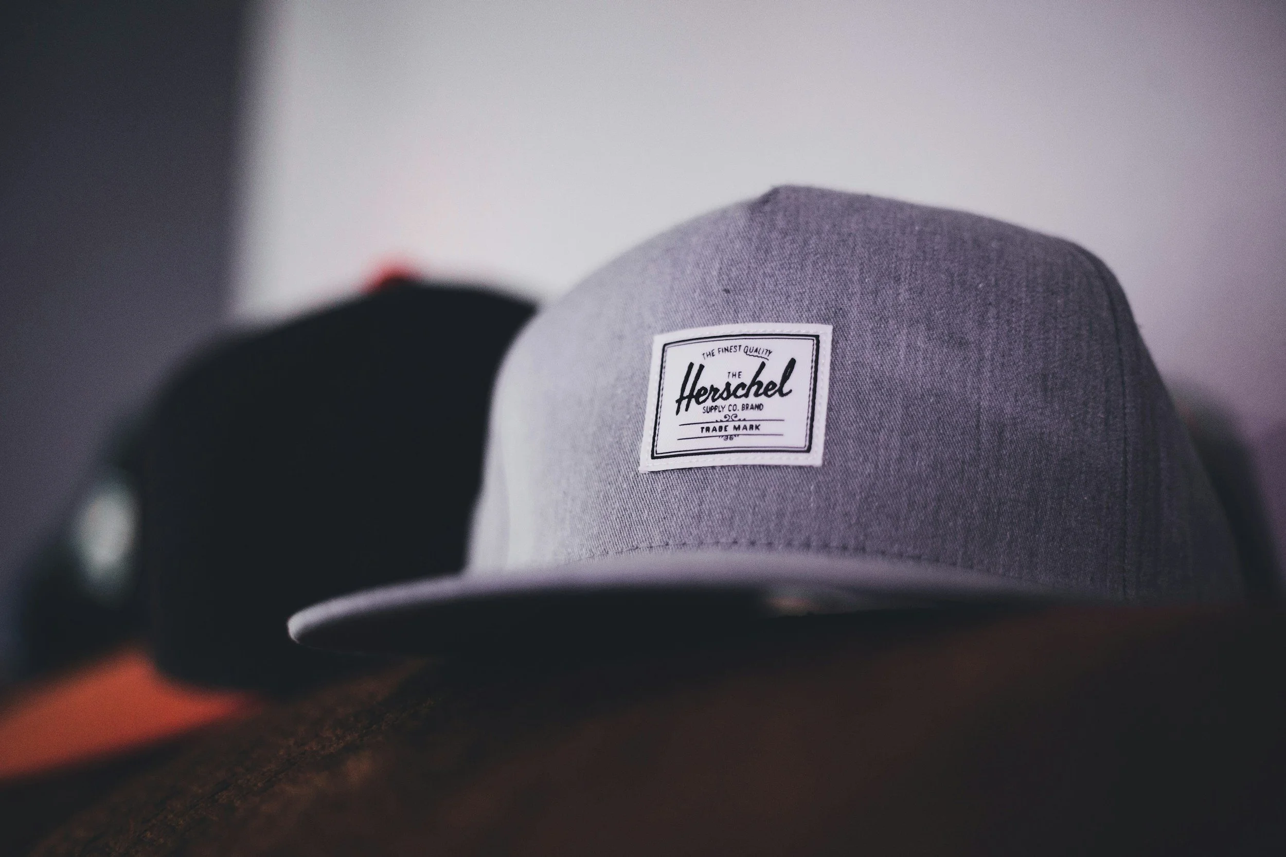 Close-up of a gray baseball cap with a black and white Herschel supply co. brand label, placed on a brown wooden surface.