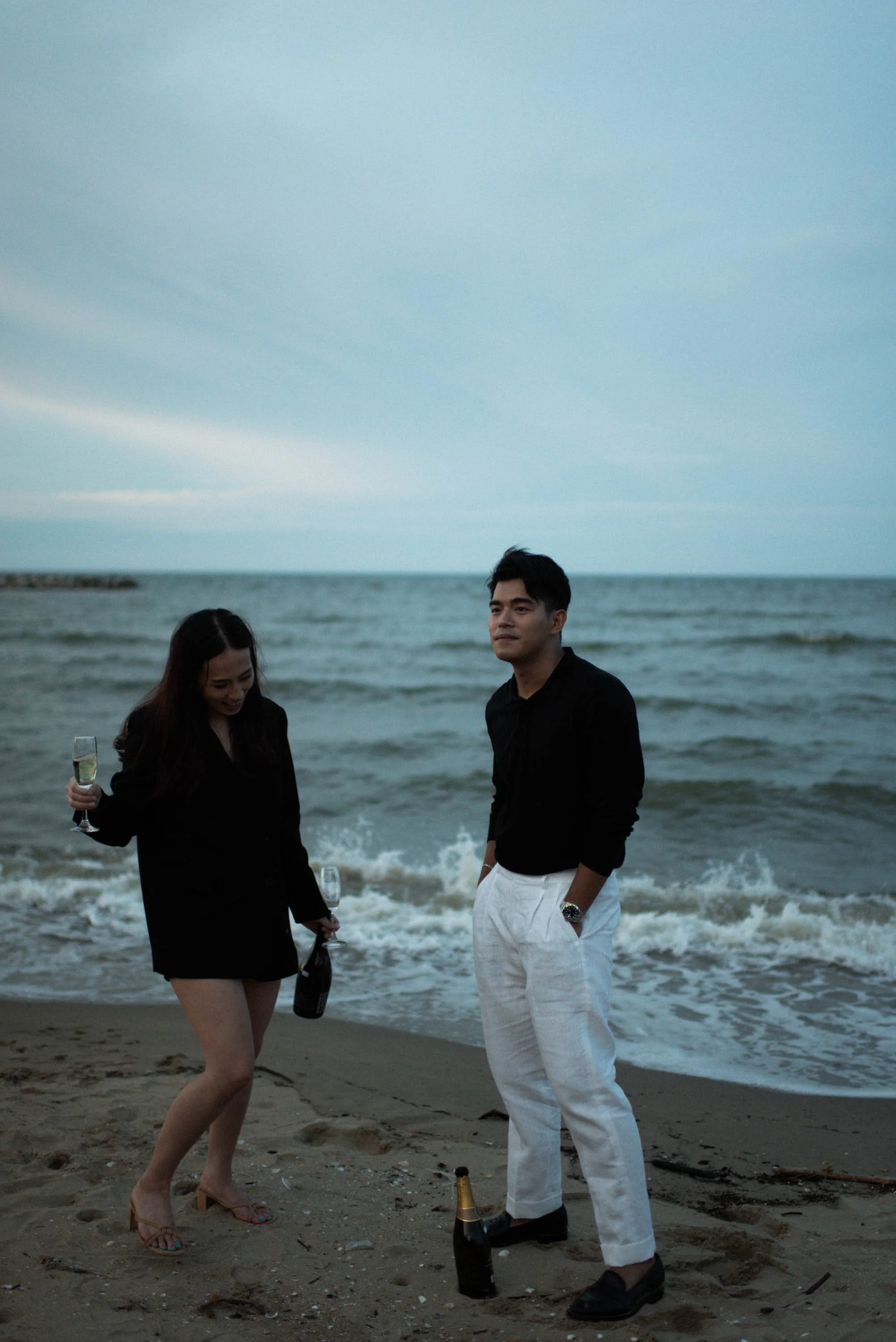 Couple enjoying champagne together by the sea at dusk.