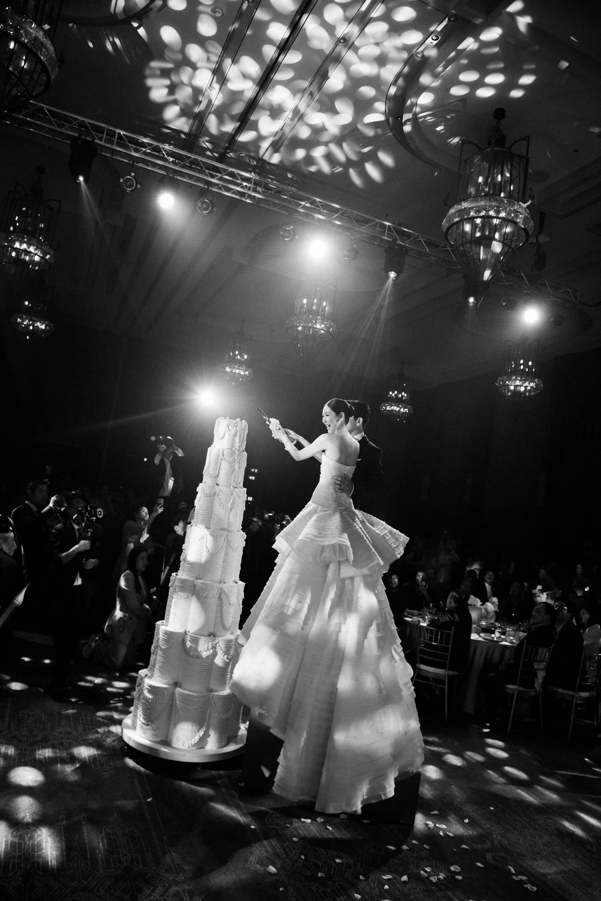 Bride and groom standing beside their wedding cake in the ballroom.