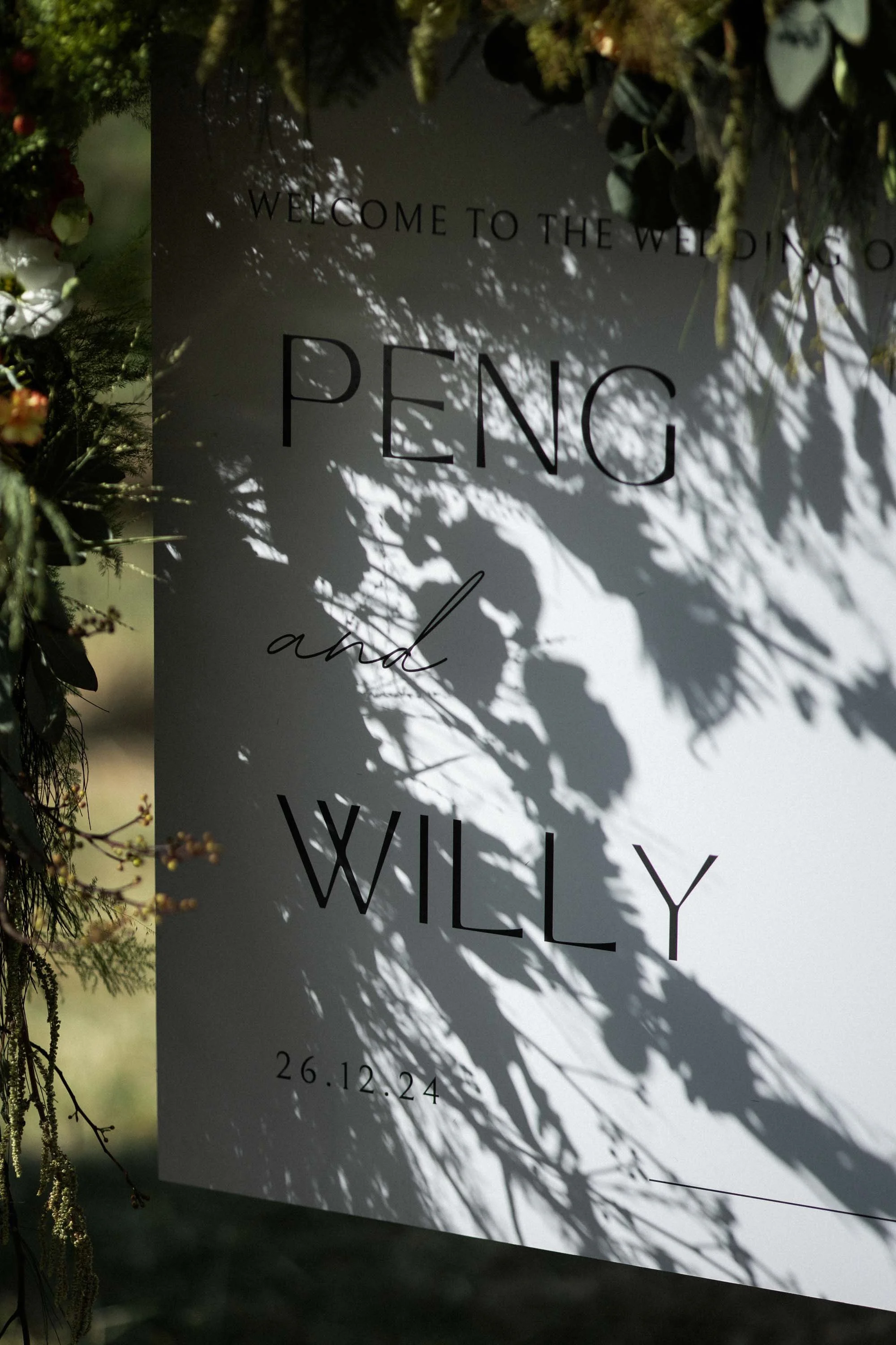 Wedding welcome sign with natural light and shadows cast by surrounding leaves.