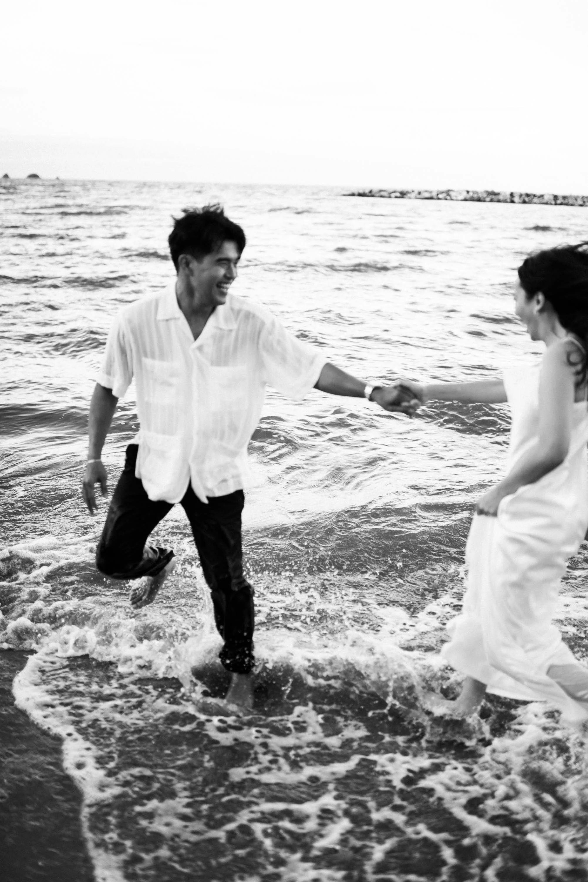 Couple running and playing in the waves along the beach.