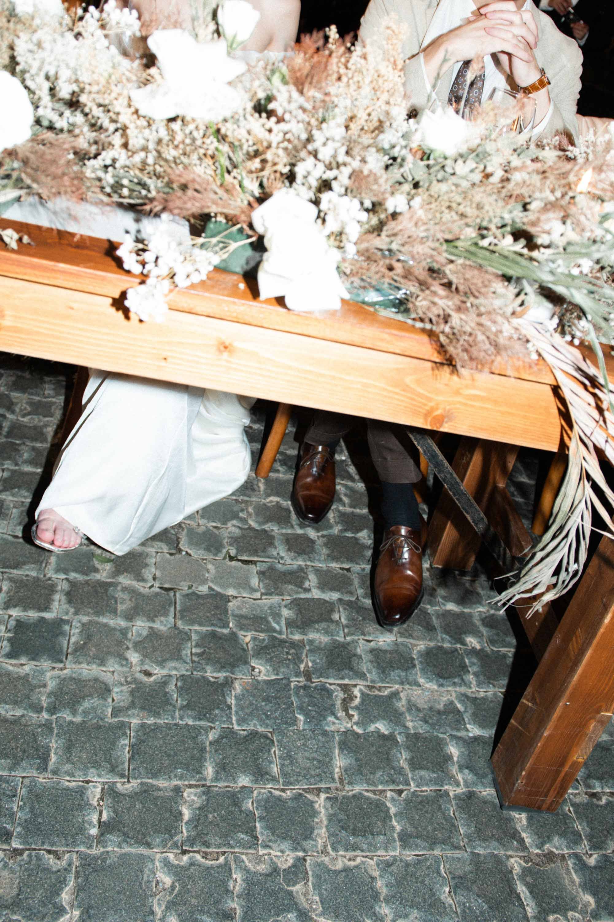 Bride and groom sitting together at their table with matching crossed legs and wedding table details.