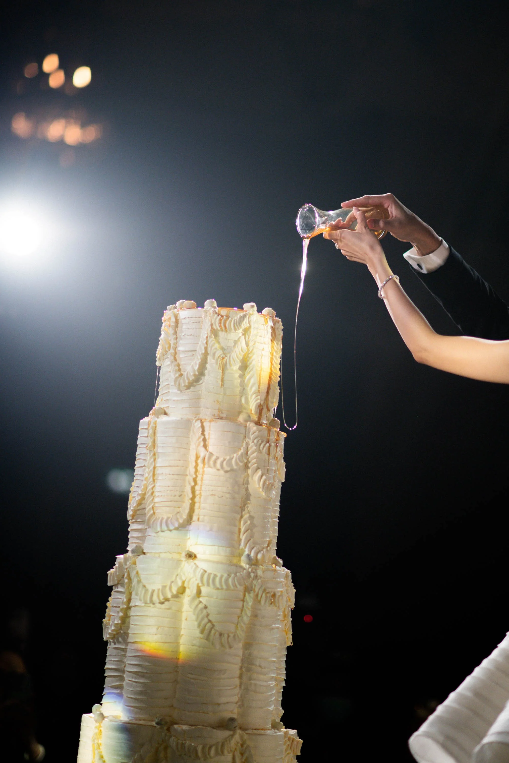 Close-up of the couple pouring honey over the wedding cake.