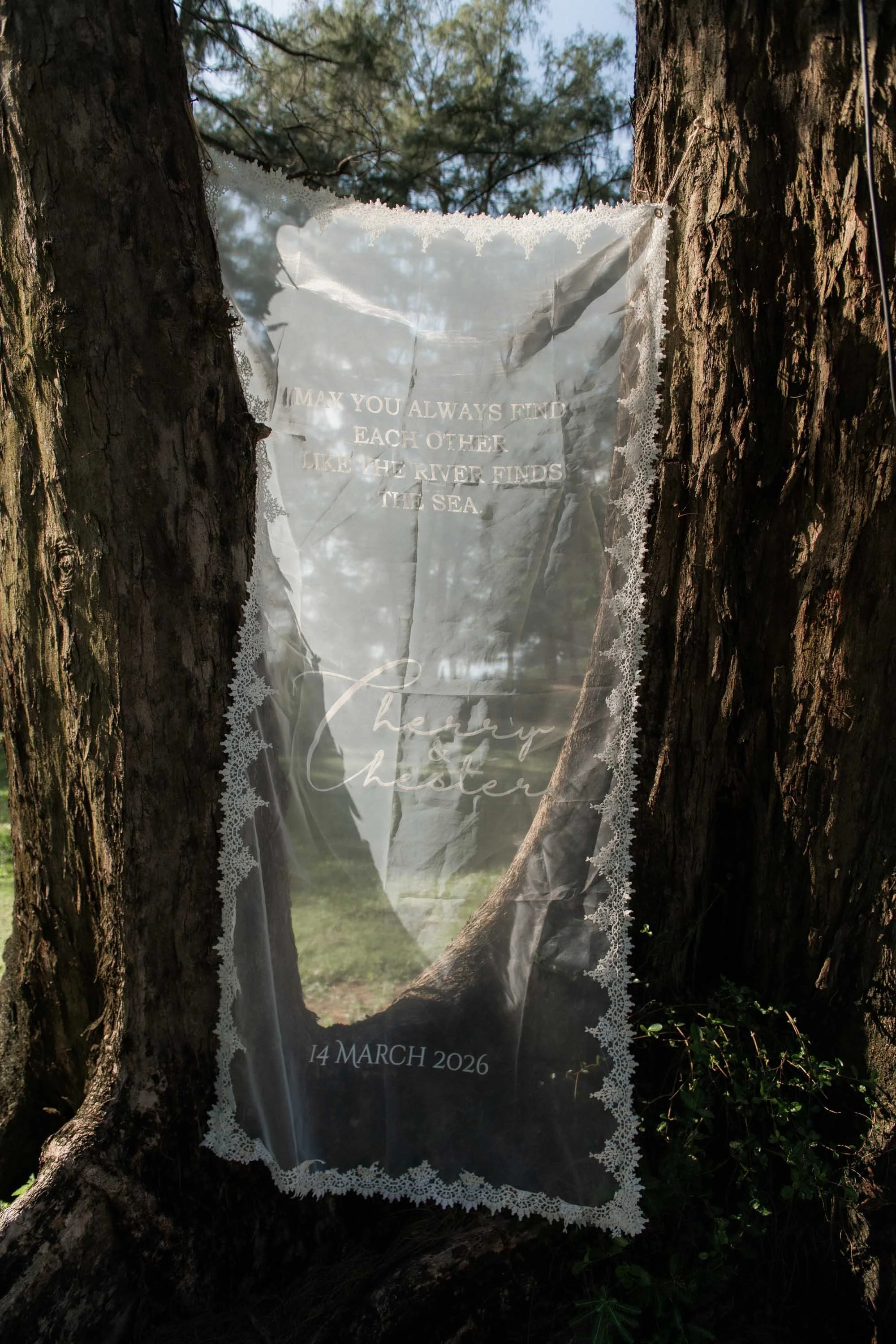 Wedding fabric sign displayed between the trees.