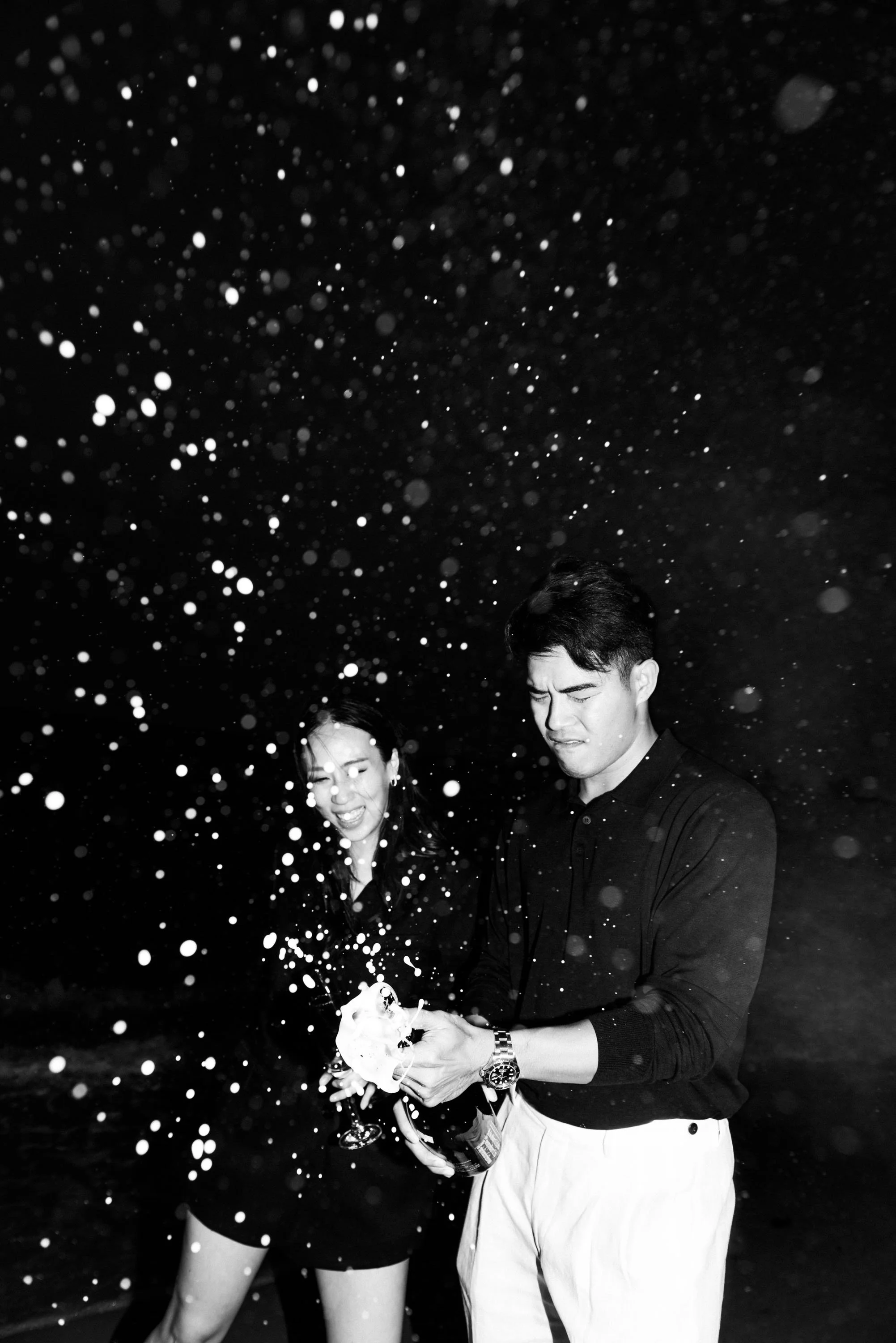 Couple opening champagne as it sprays into the air on the beach.